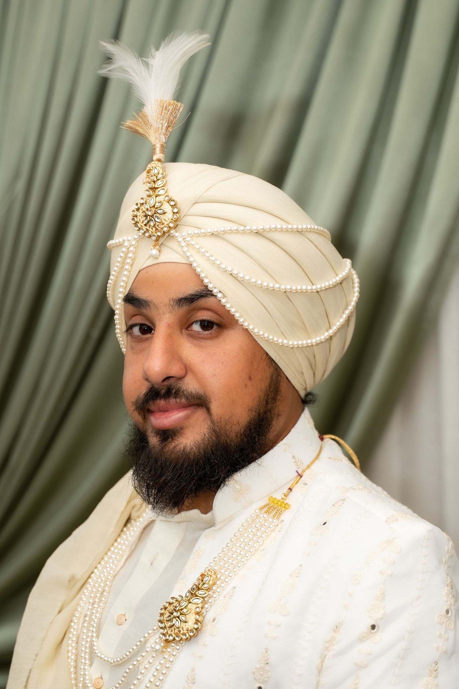 A person wearing traditional Indian wedding attire including a white sherwani and cream turban with pearl details.