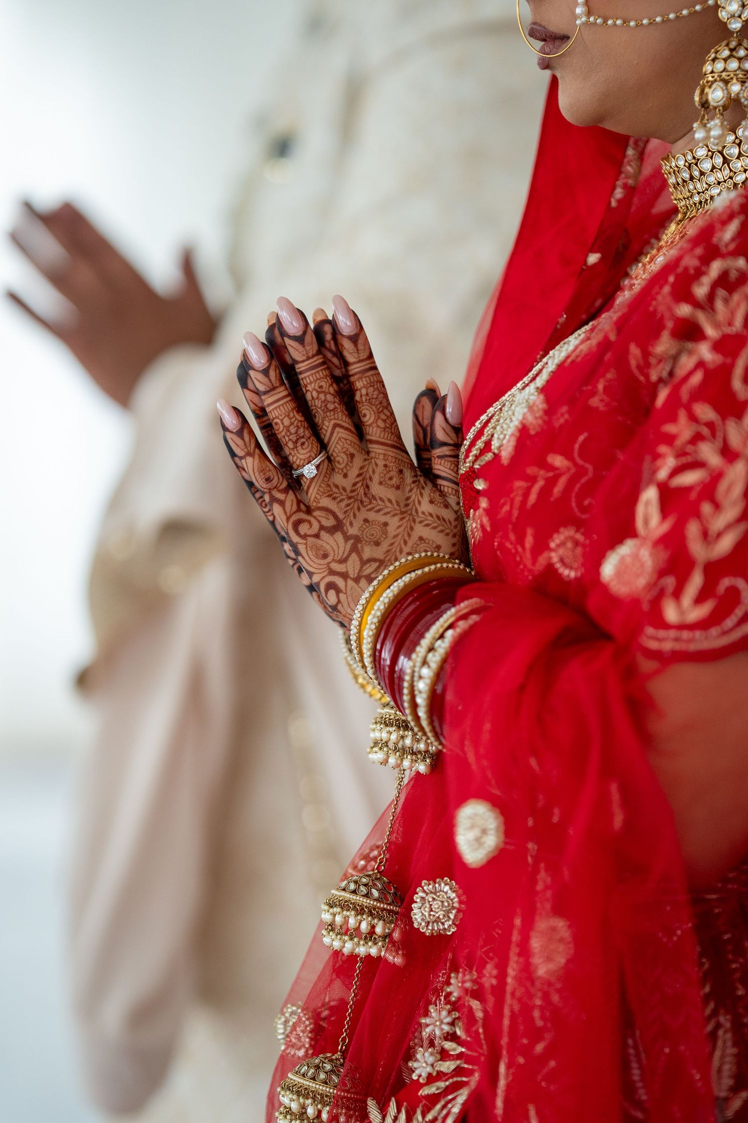 Close-up of intricate henna designs on hands with gold bangles and red traditional wedding attire.