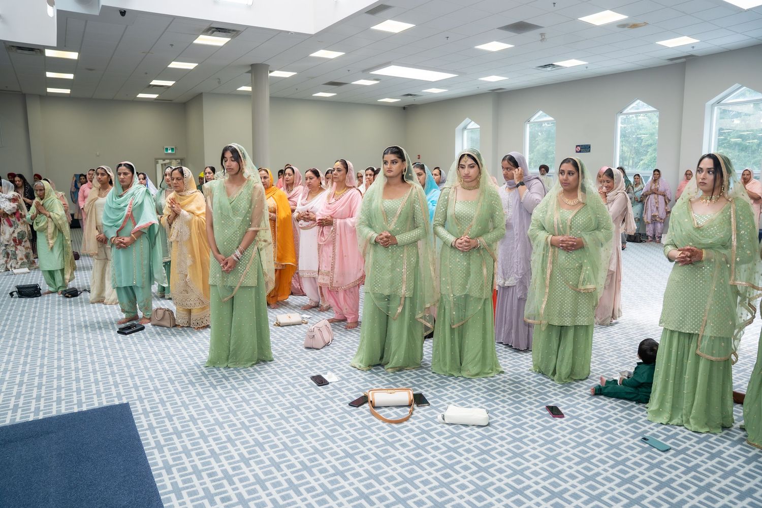 A group of bridesmaids in matching mint green outfits stand together in a line at a wedding ceremony.