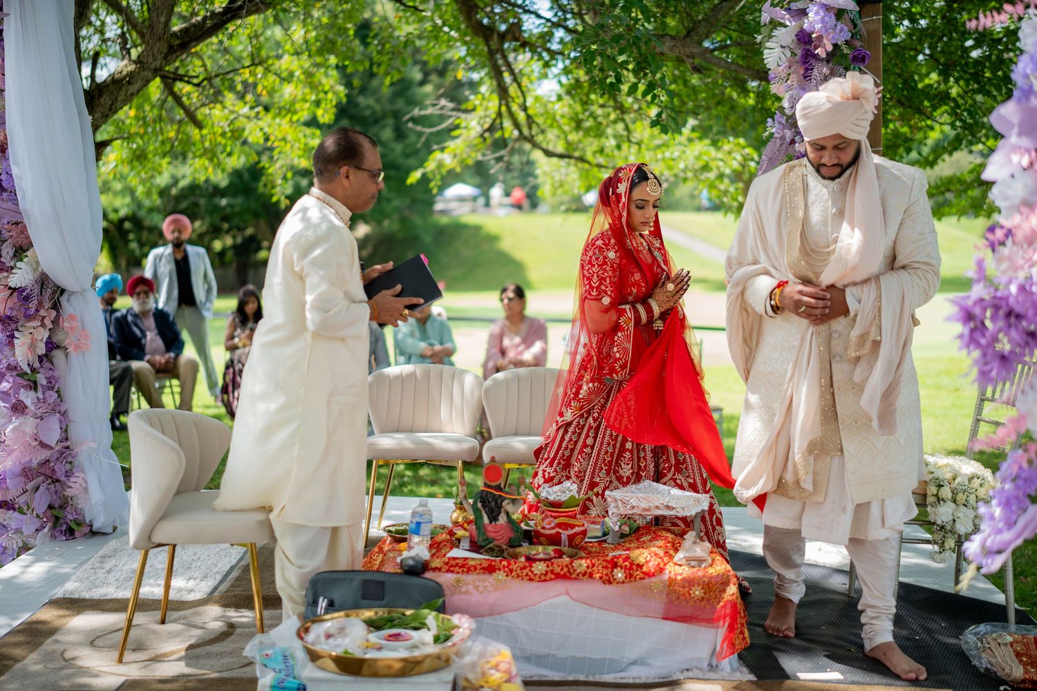 Garden wedding ceremony with purple floral decorations and natural greenery backdrop.