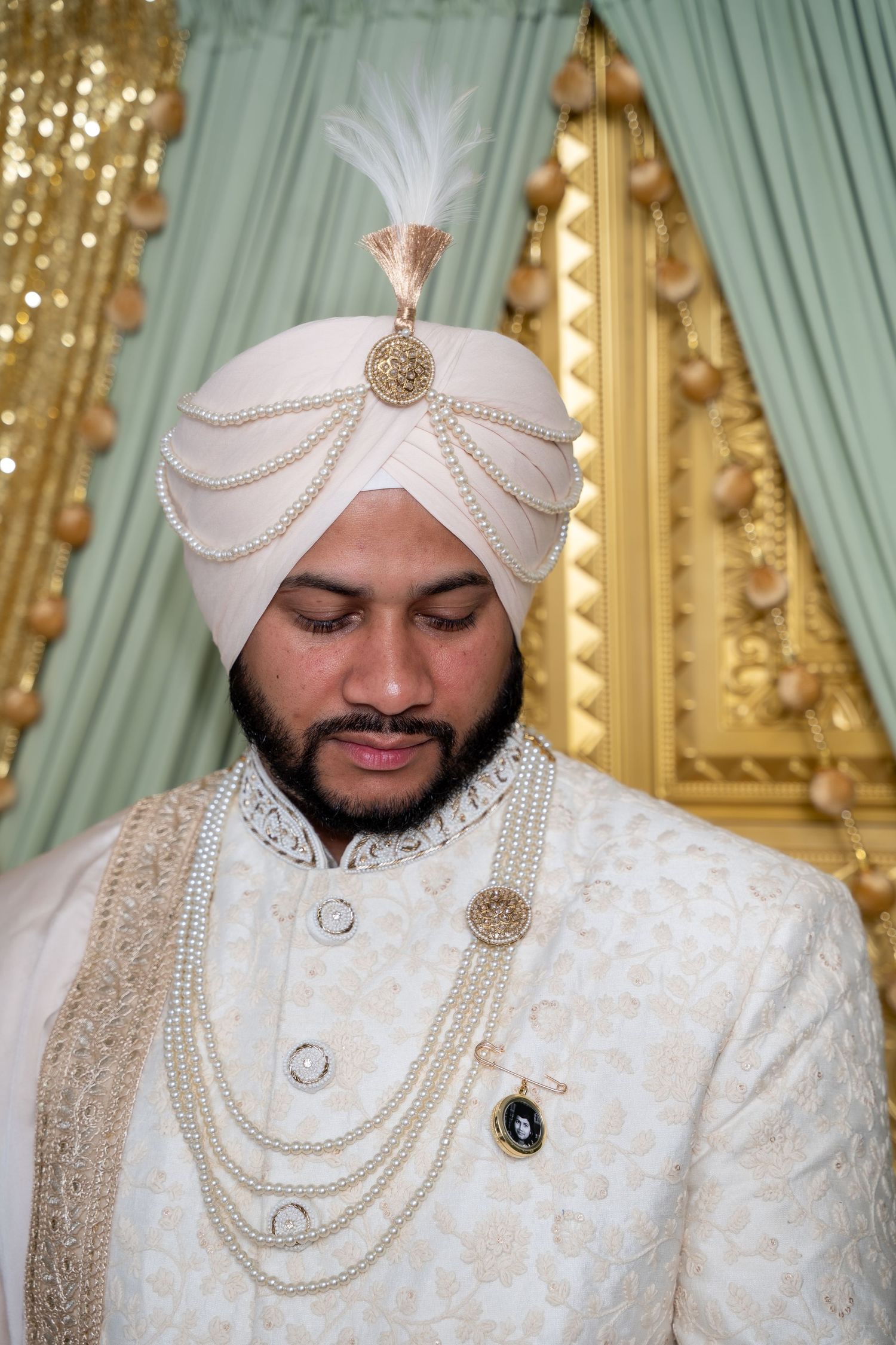 Traditional Sikh groom wearing an ornate white sherwani with pearl necklaces and embellished turban.