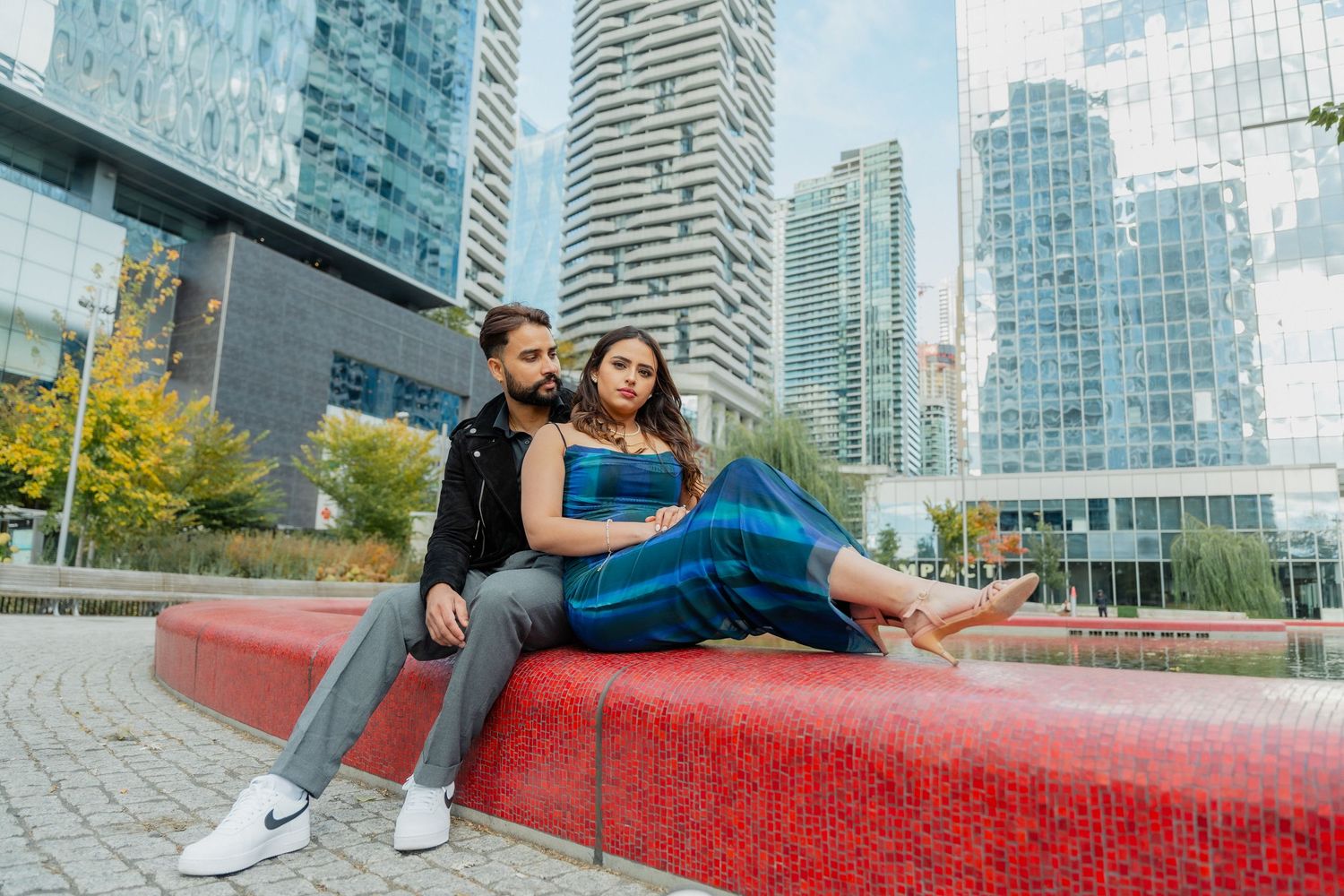 Two people relaxing on a red bench in an urban setting with modern glass skyscrapers in the background.