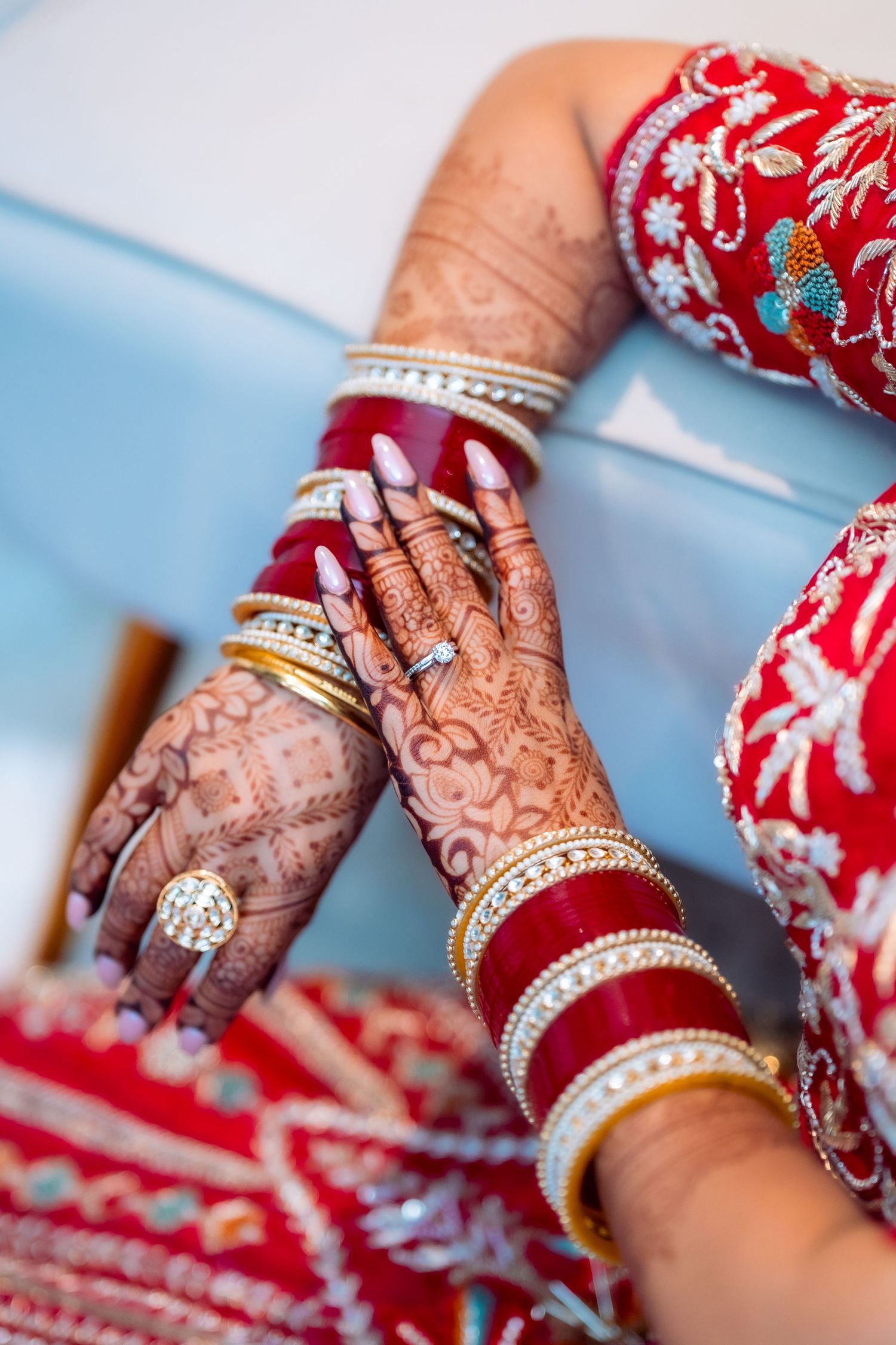 Intricate henna designs and gold bangles adorning hands against a red and silver embroidered dress.