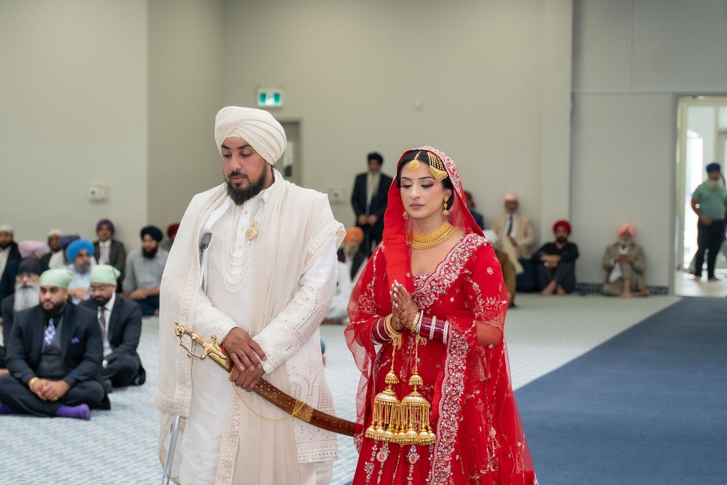 A traditional Indian wedding ceremony with the couple in red and white traditional attire at an indoor venue.