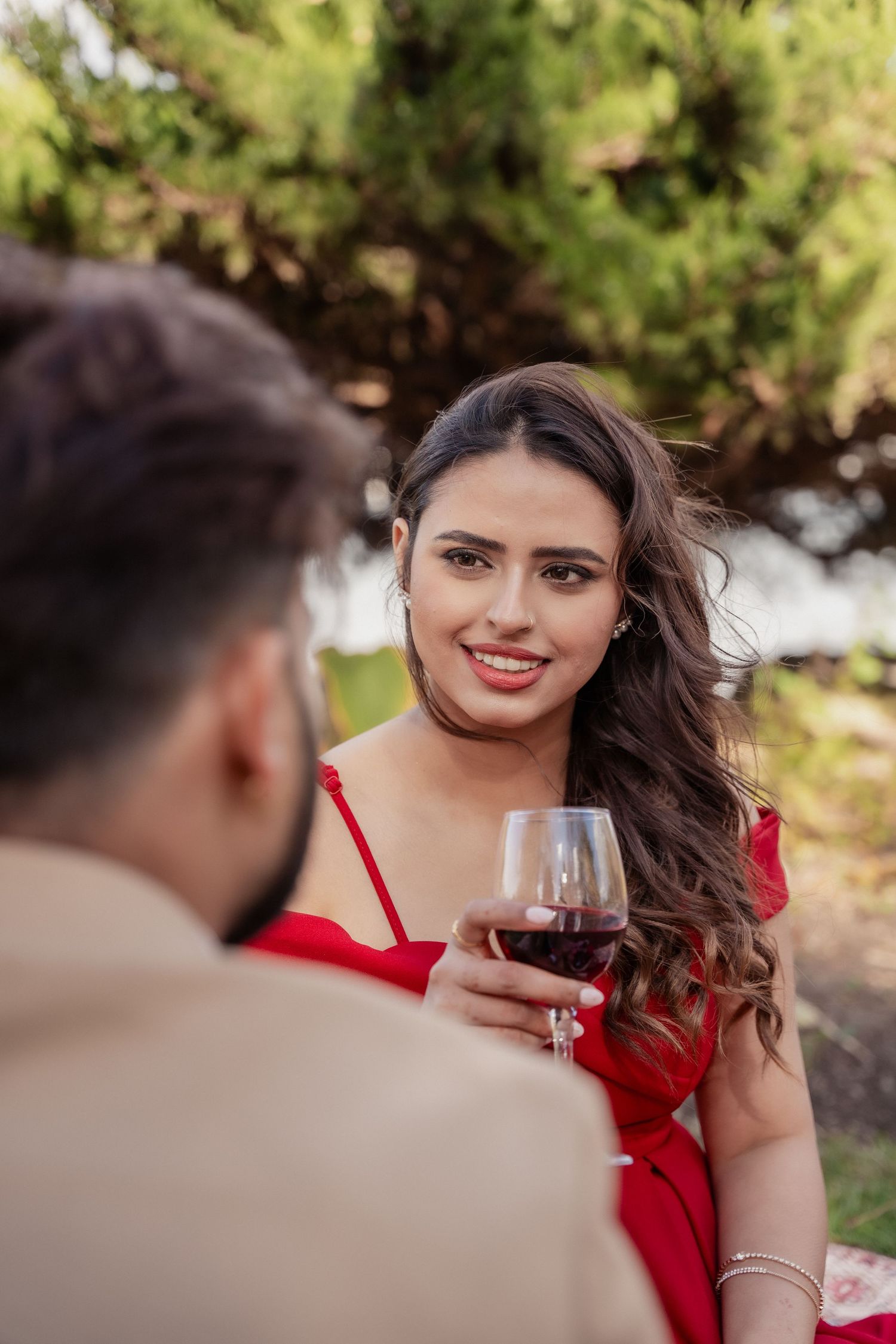 A romantic wine tasting scene outdoors with a person in a red dress holding a glass of red wine.