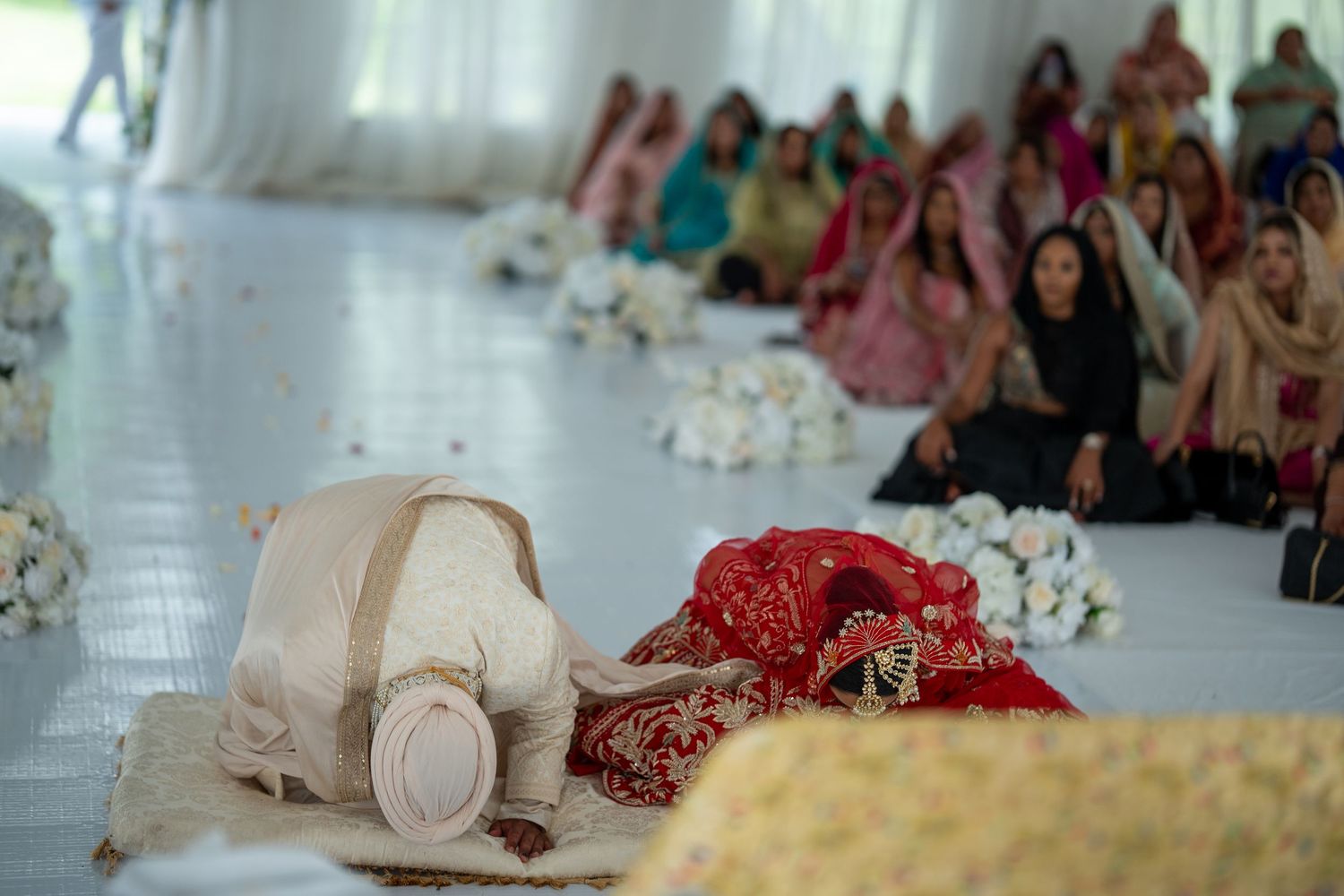 Wedding ceremony guests seated on floor in traditional Indian attire at an indoor venue.