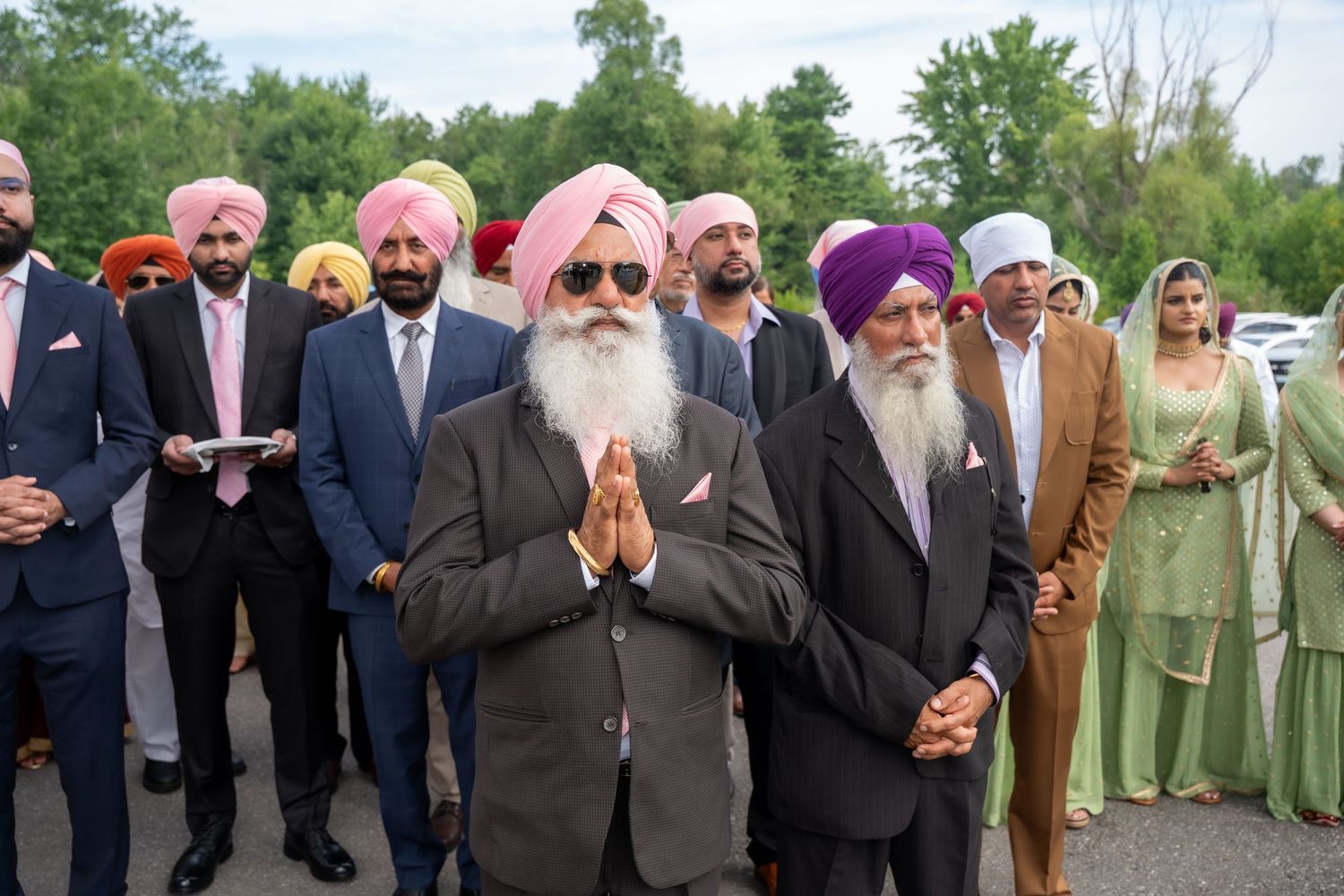 A group of people in formal attire gather outdoors at a social event wearing traditional Sikh clothing and turbans.