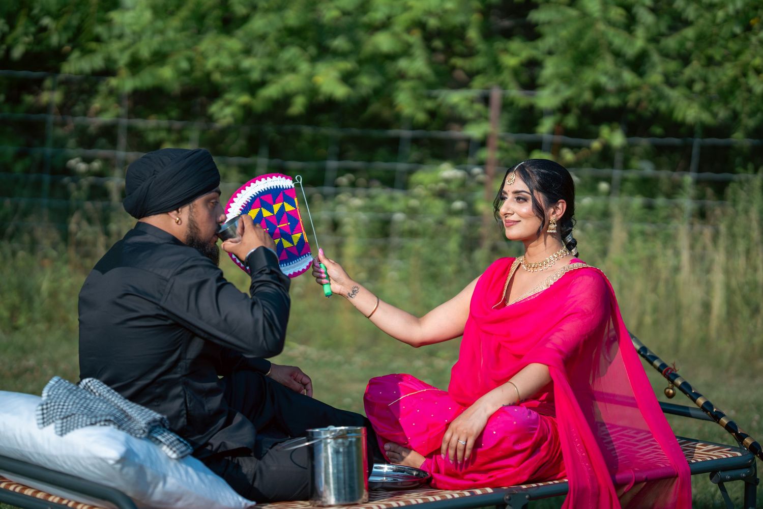 A couple in a park setting poses for a series of engagement photos with the woman wearing a bright pink dress.