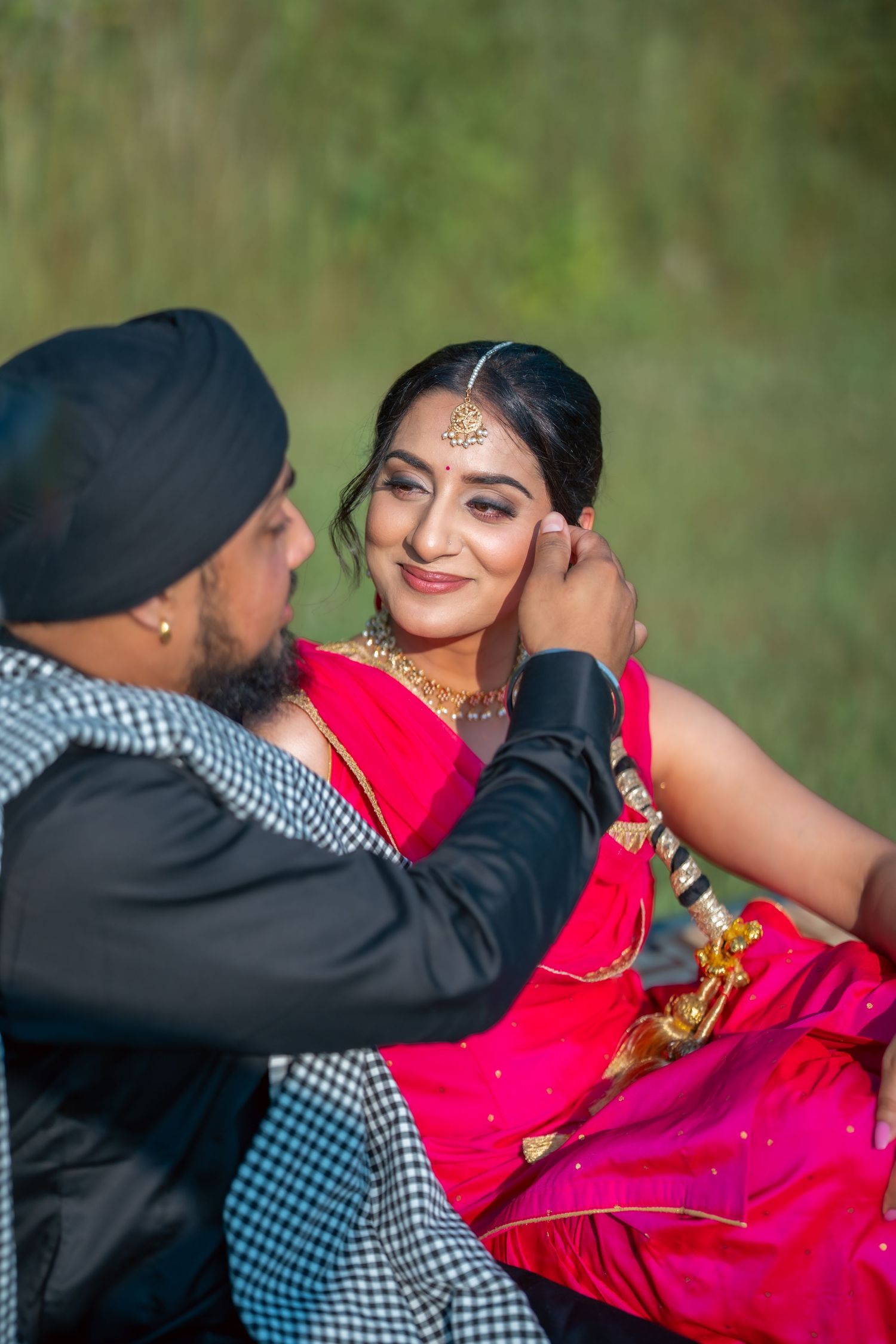A romantic outdoor photoshoot showing a couple in traditional Indian attire with vibrant red and pink colors.