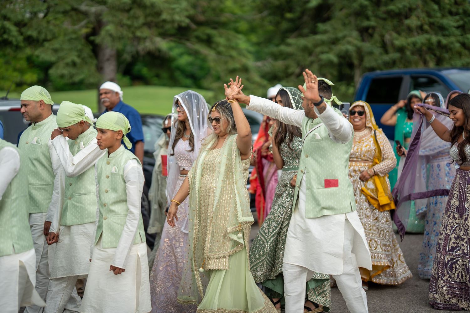 Large group of wedding guests in light colored traditional attire gathered outdoors.