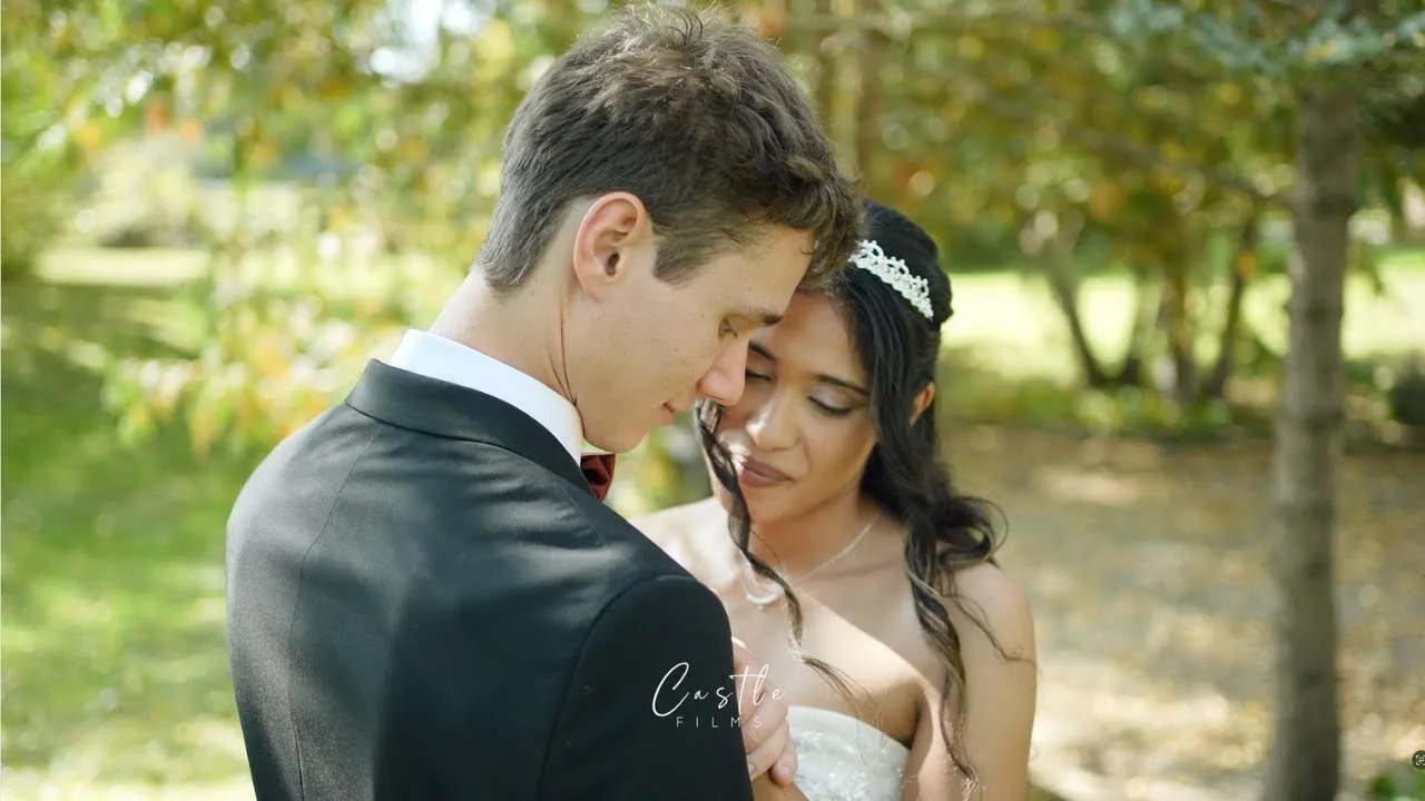 A bride and groom share an intimate moment outdoors, surrounded by lush green trees on their wedding day.