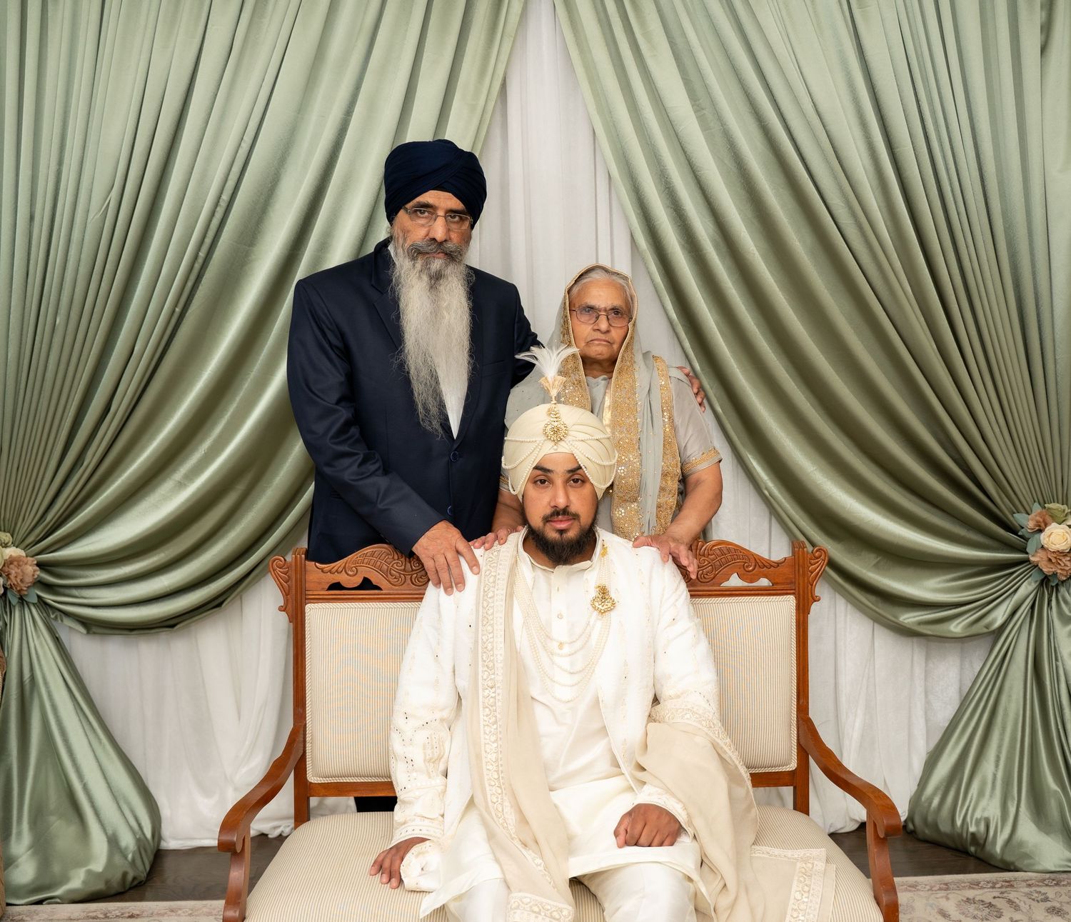 Traditional Sikh wedding ceremony with cream and gold decor against sage green curtain backdrop.