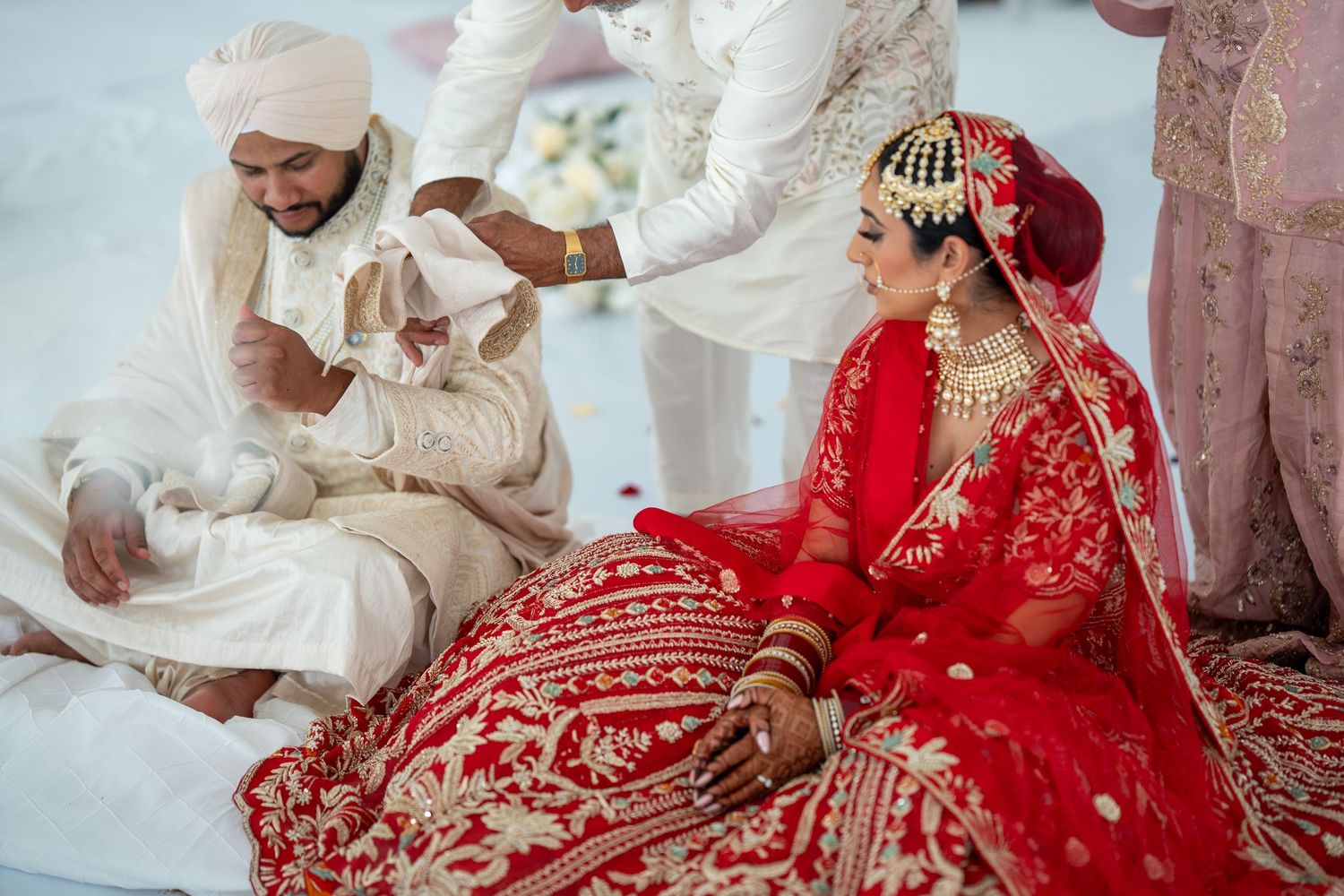 Traditional Indian wedding ceremony with guests seated in white and red attire.
