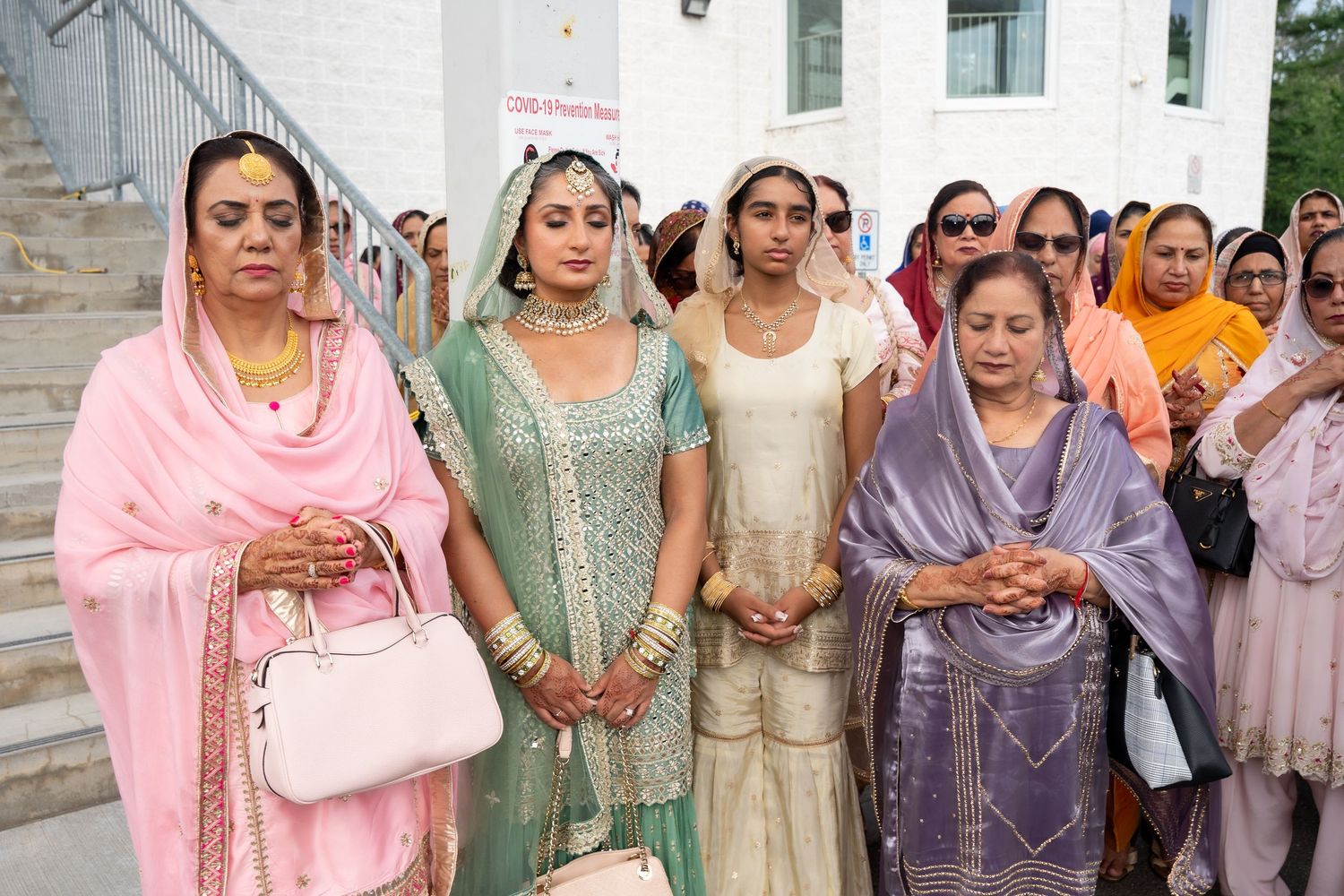 Wedding guests in traditional South Asian attire gather outside for a group photo.