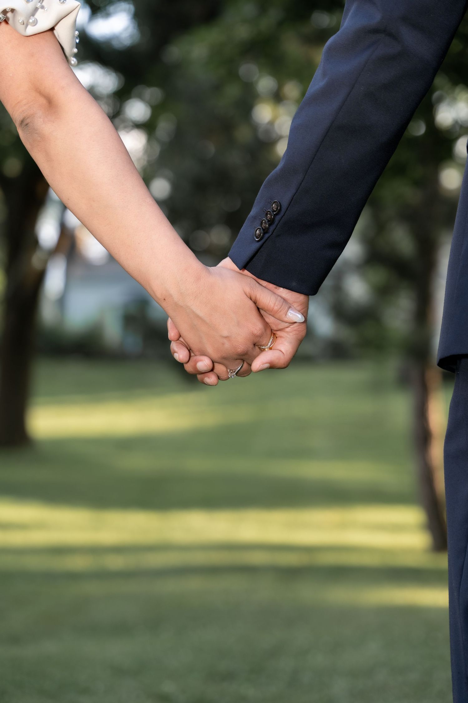 Close-up shot of two people holding hands in formal attire against a blurred green outdoor background.