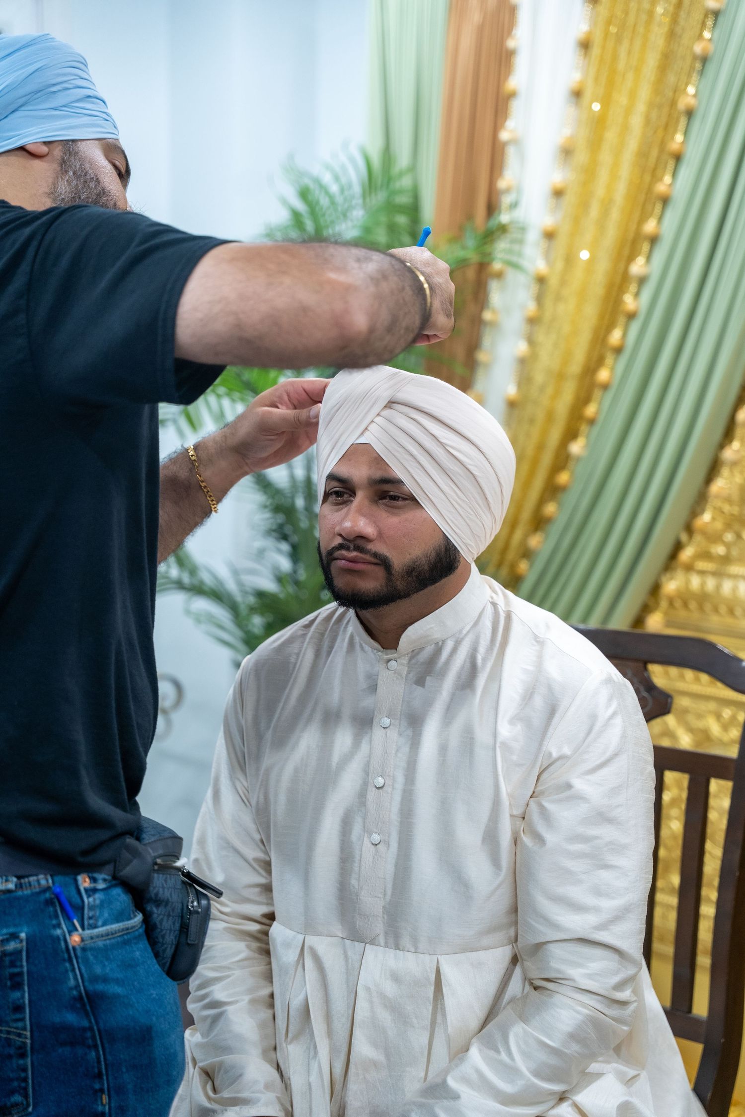 A groom getting his traditional white turban adjusted during a Sikh wedding preparation ceremony.