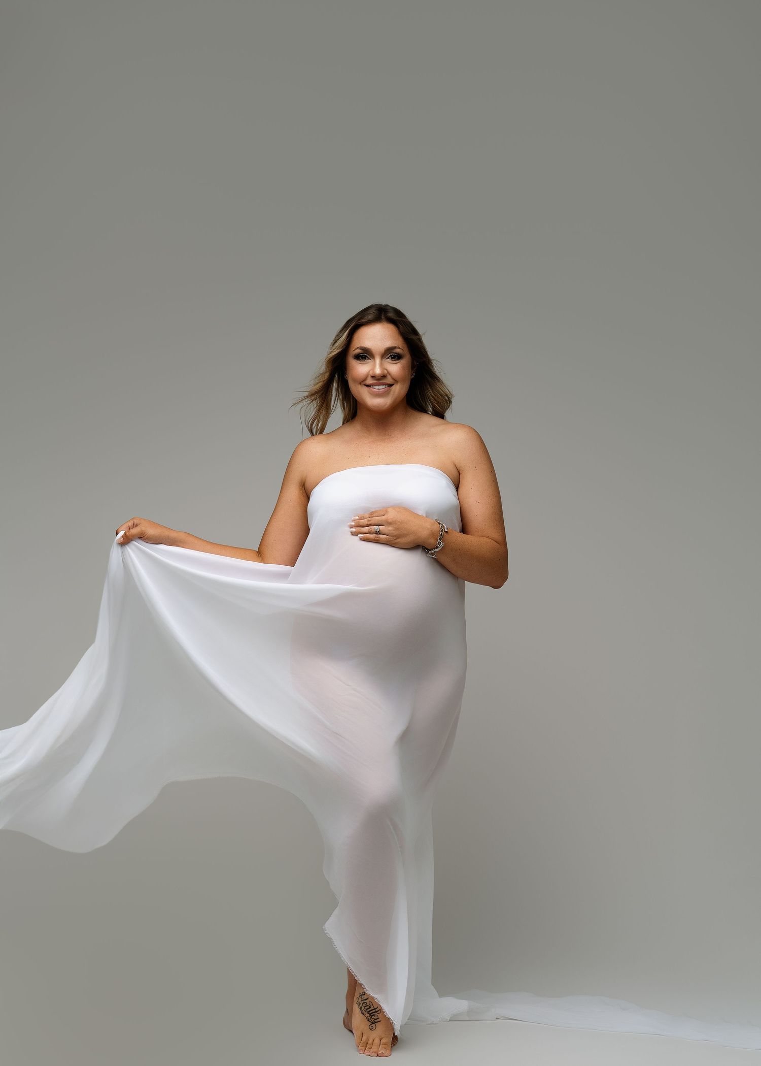 Studio maternity session with ethereal white fabric creating flowing movement.