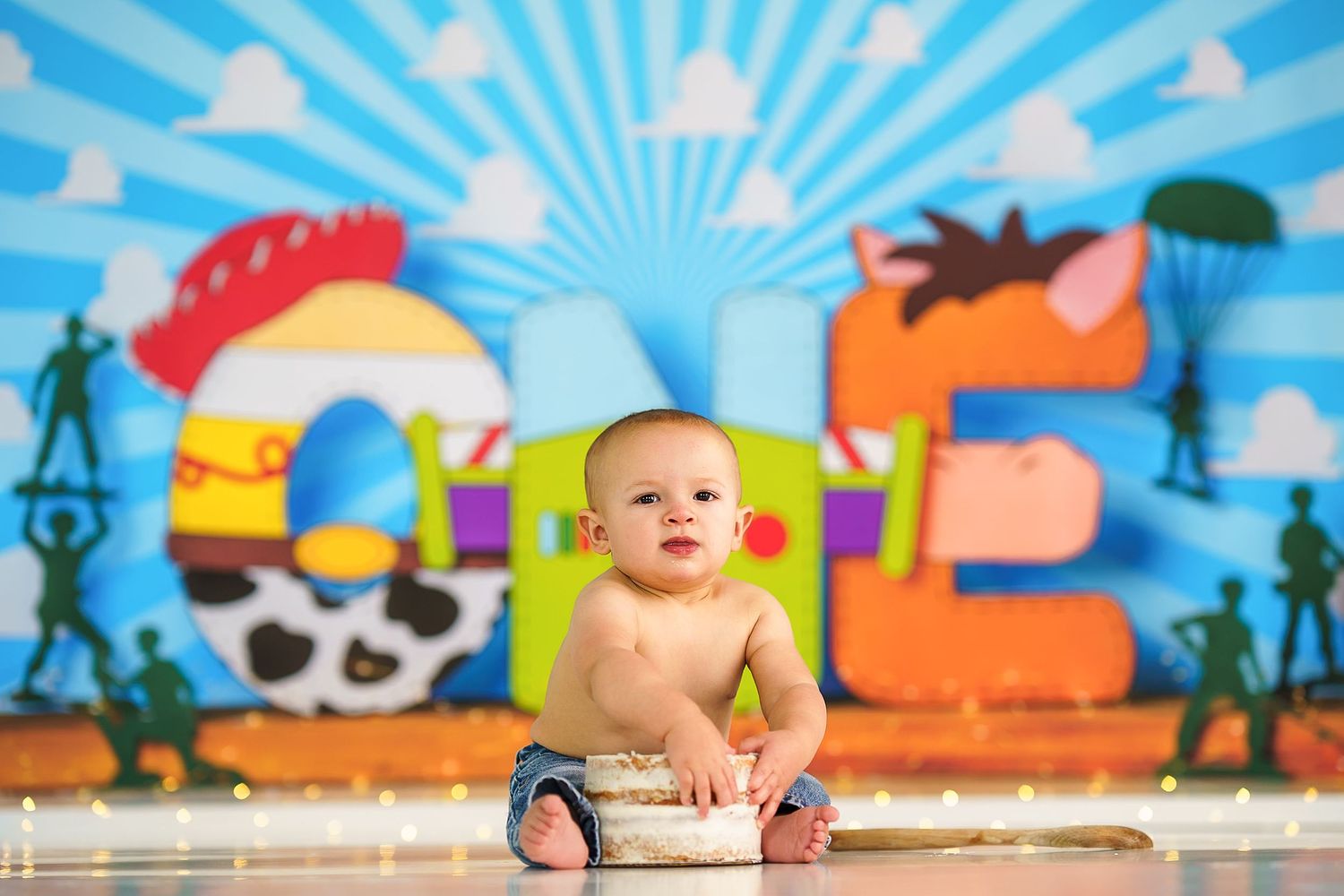 Happy baby in denim sitting against bright blue background with cartoon decorations.