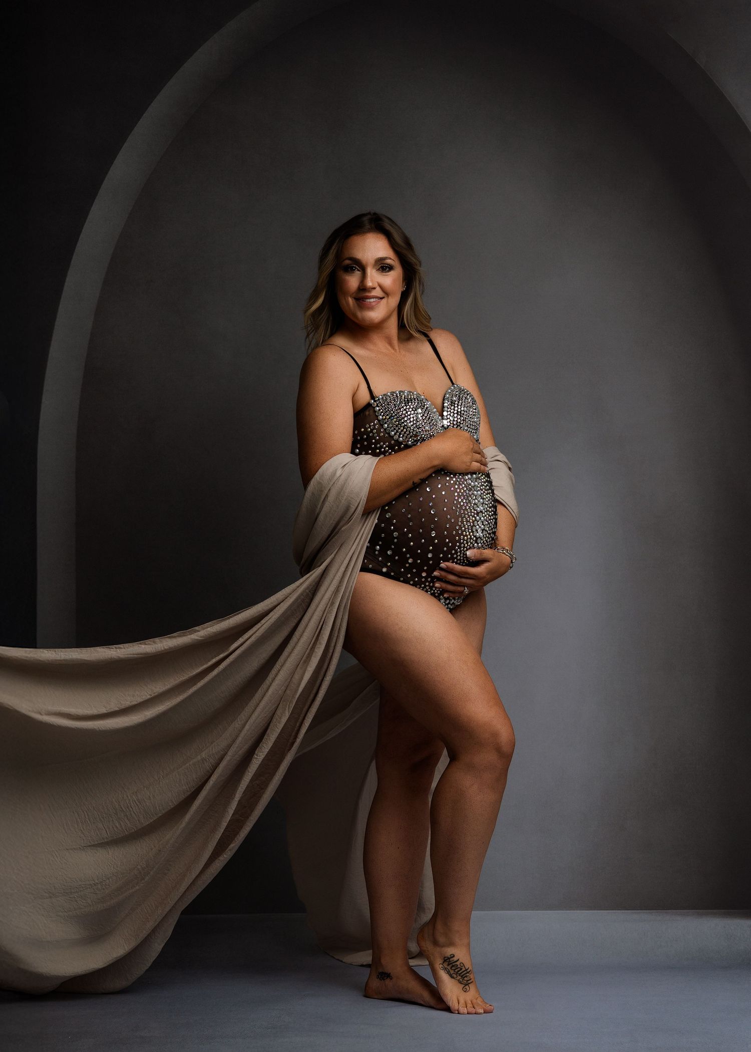 Artistic maternity portrait with flowing beige fabric in dramatic lighting.