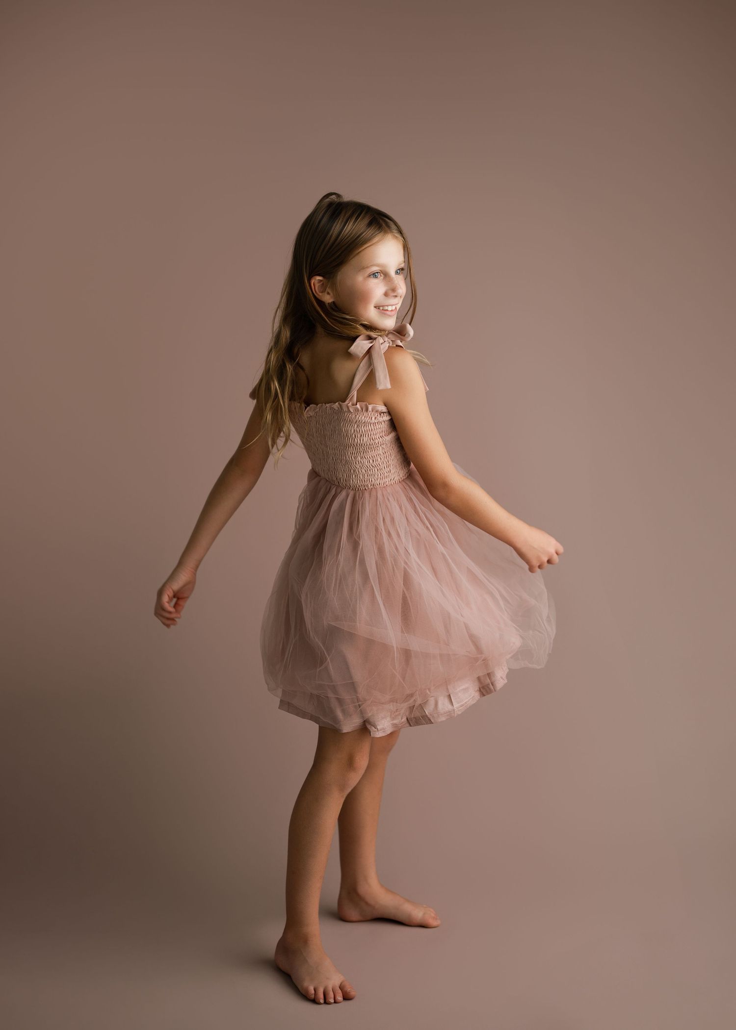 Young dancer twirls and poses in pink tulle dress during studio photoshoot.