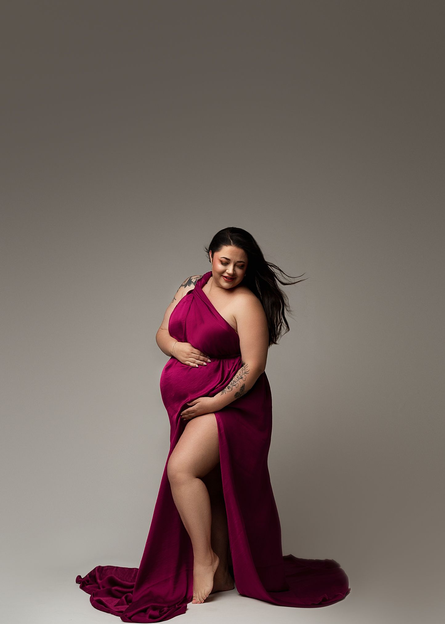 Elegant portrait series in flowing burgundy dress against grey studio backdrop.