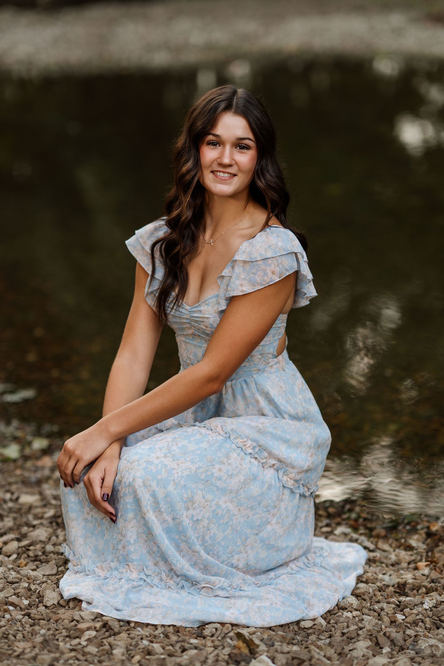 Subject in light blue dress sits gracefully on rocky riverbank.