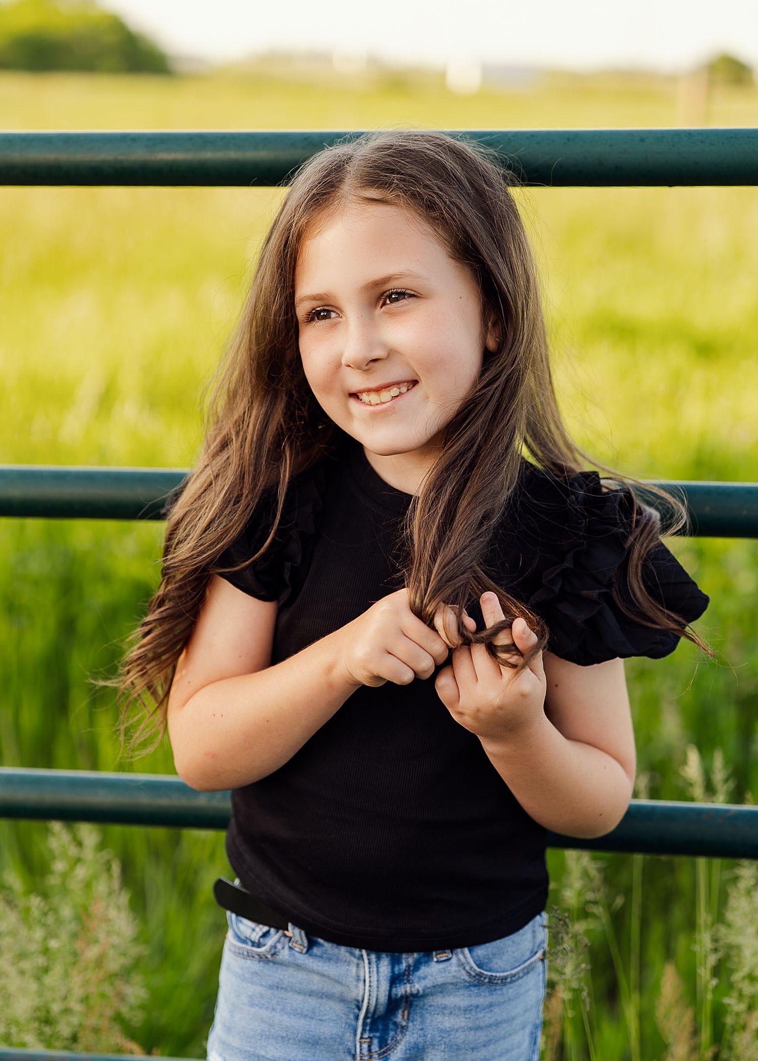 Playful poses by metal fence with green summer field in background.