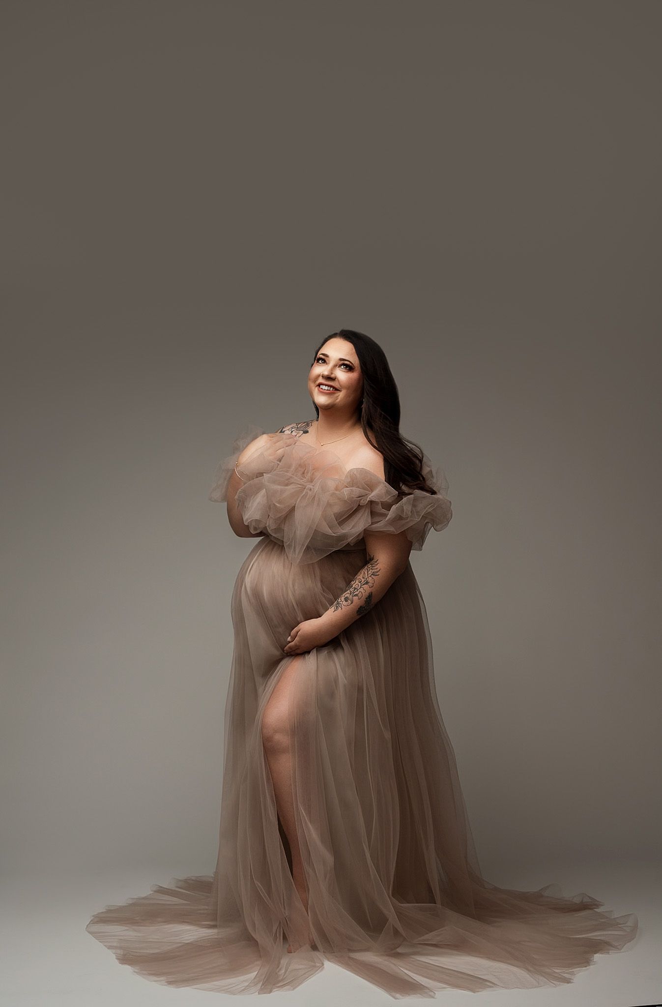 Dreamy champagne tulle gown with dramatic ruffled shoulders in sophisticated studio portrait.