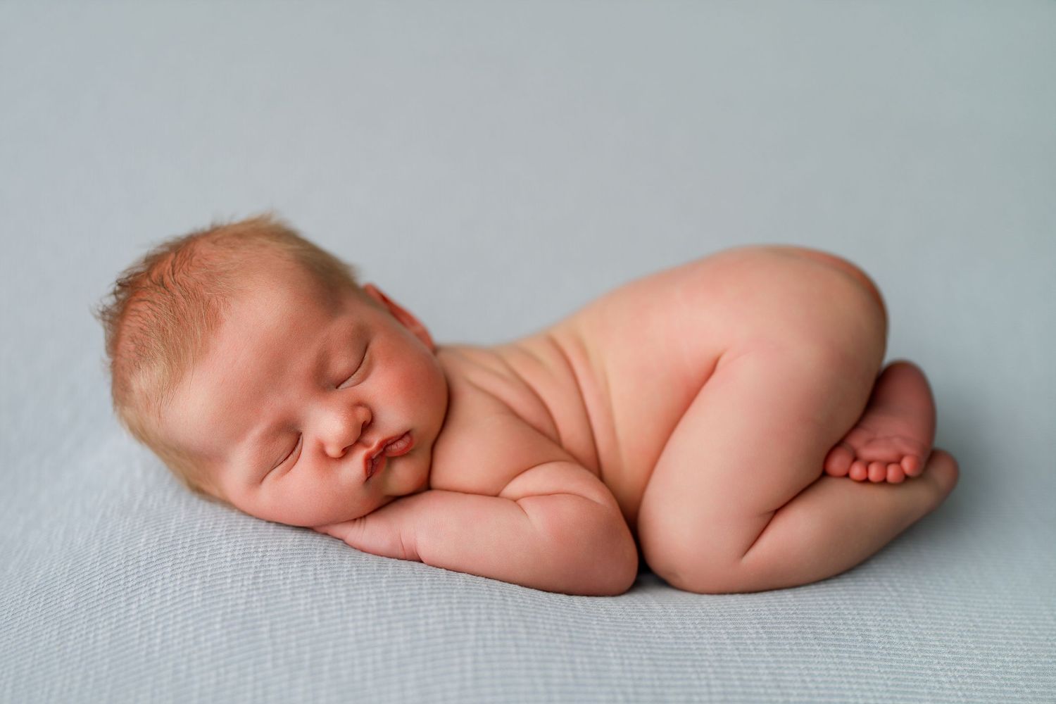 Artistic newborn photography pose showing sleeping baby on light gray backdrop.