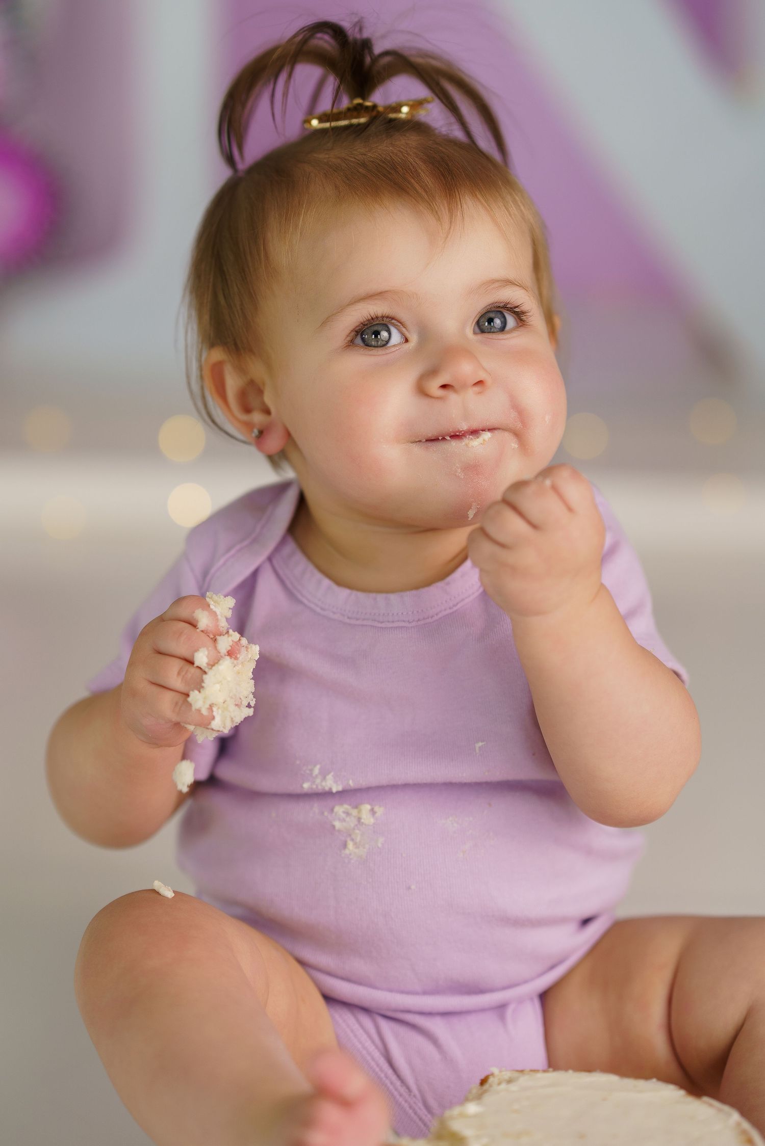 Baby wearing purple outfit exploring cake during milestone photo session.