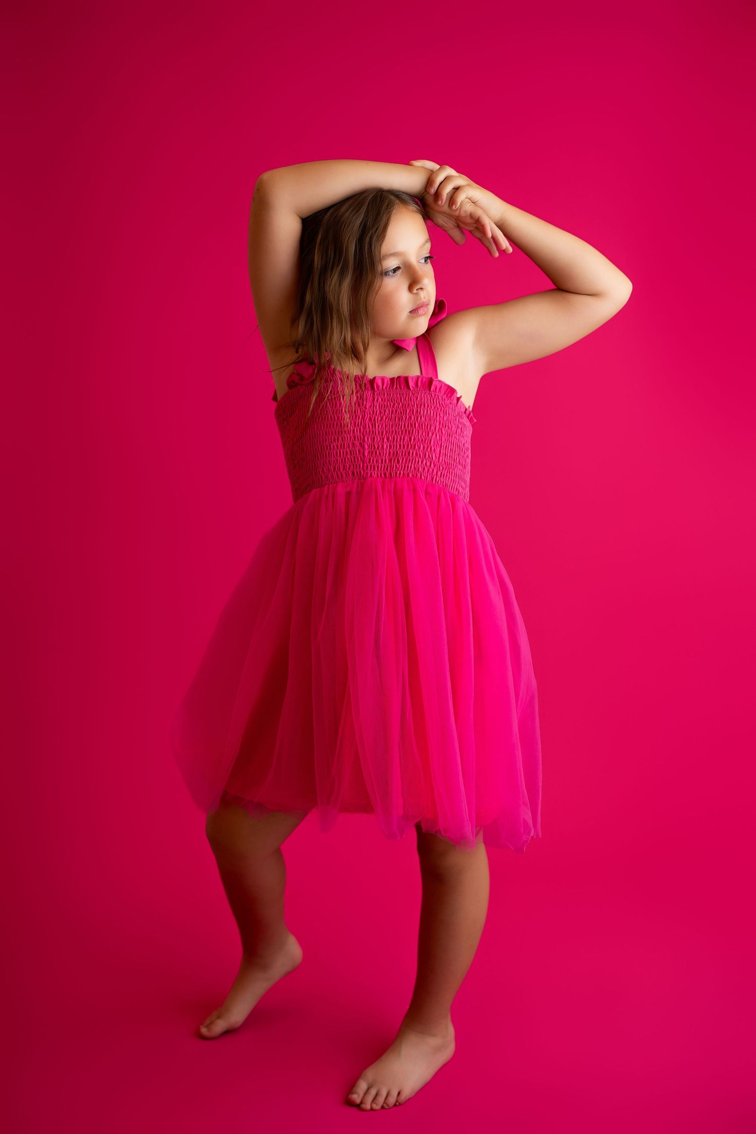 A child strikes playful poses in a flowy pink dress against a bright backdrop.