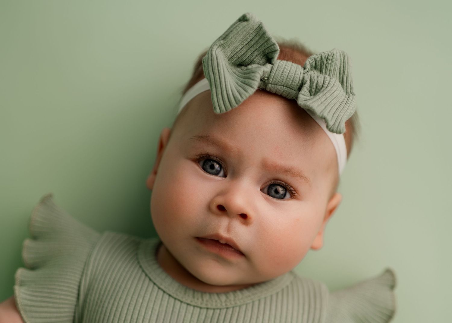 Baby portrait with mint green bow against soft pastel background.