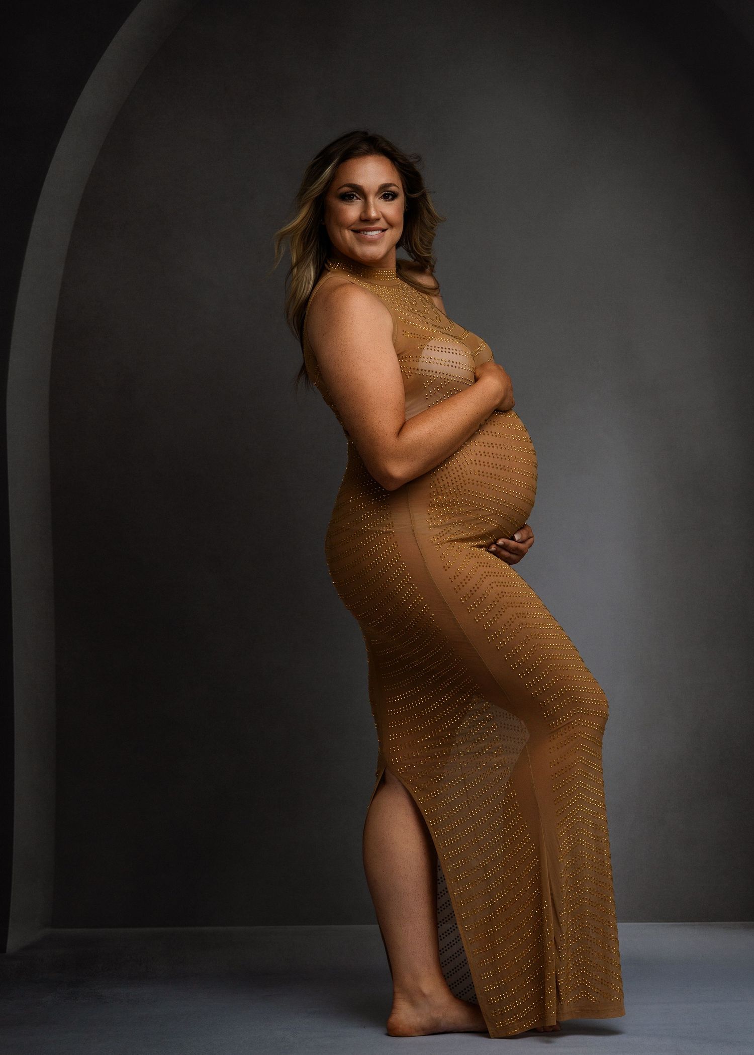 Studio maternity session featuring poses in a fitted caramel-colored dress.