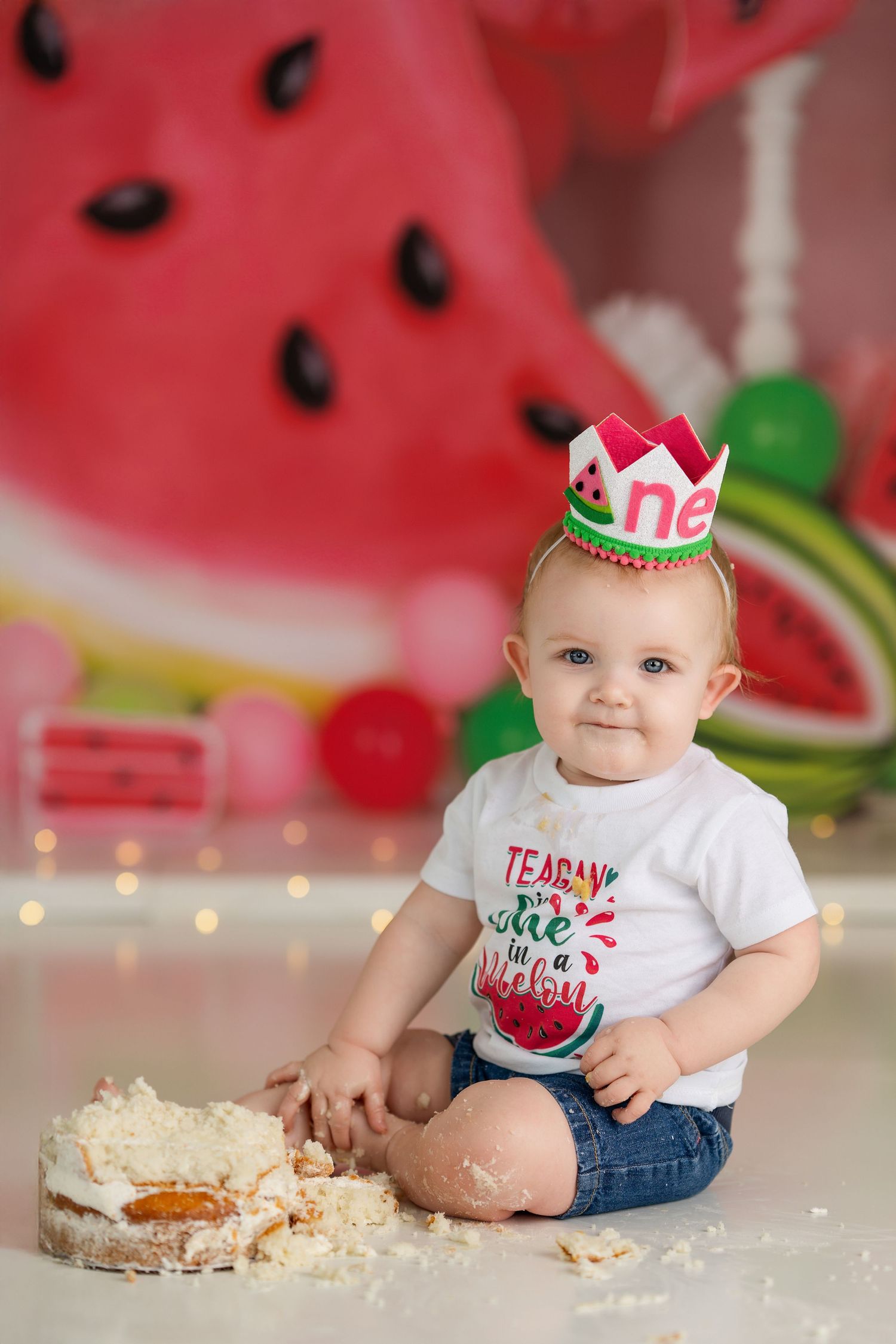 Cake smash photo session with watermelon-themed decorations and party crown.