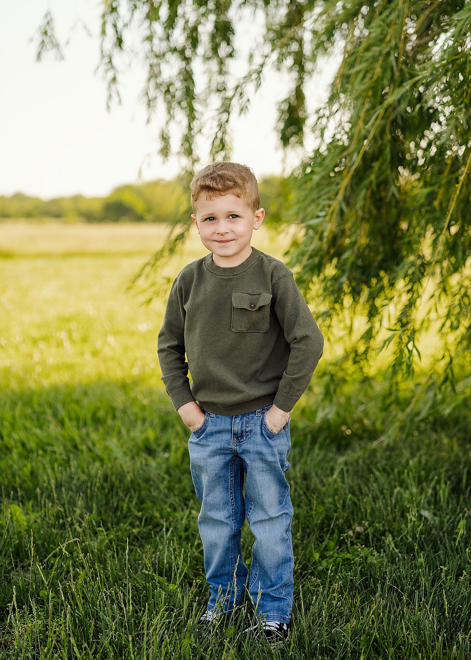Outdoor portrait in olive green sweater and jeans against natural willow tree backdrop.
