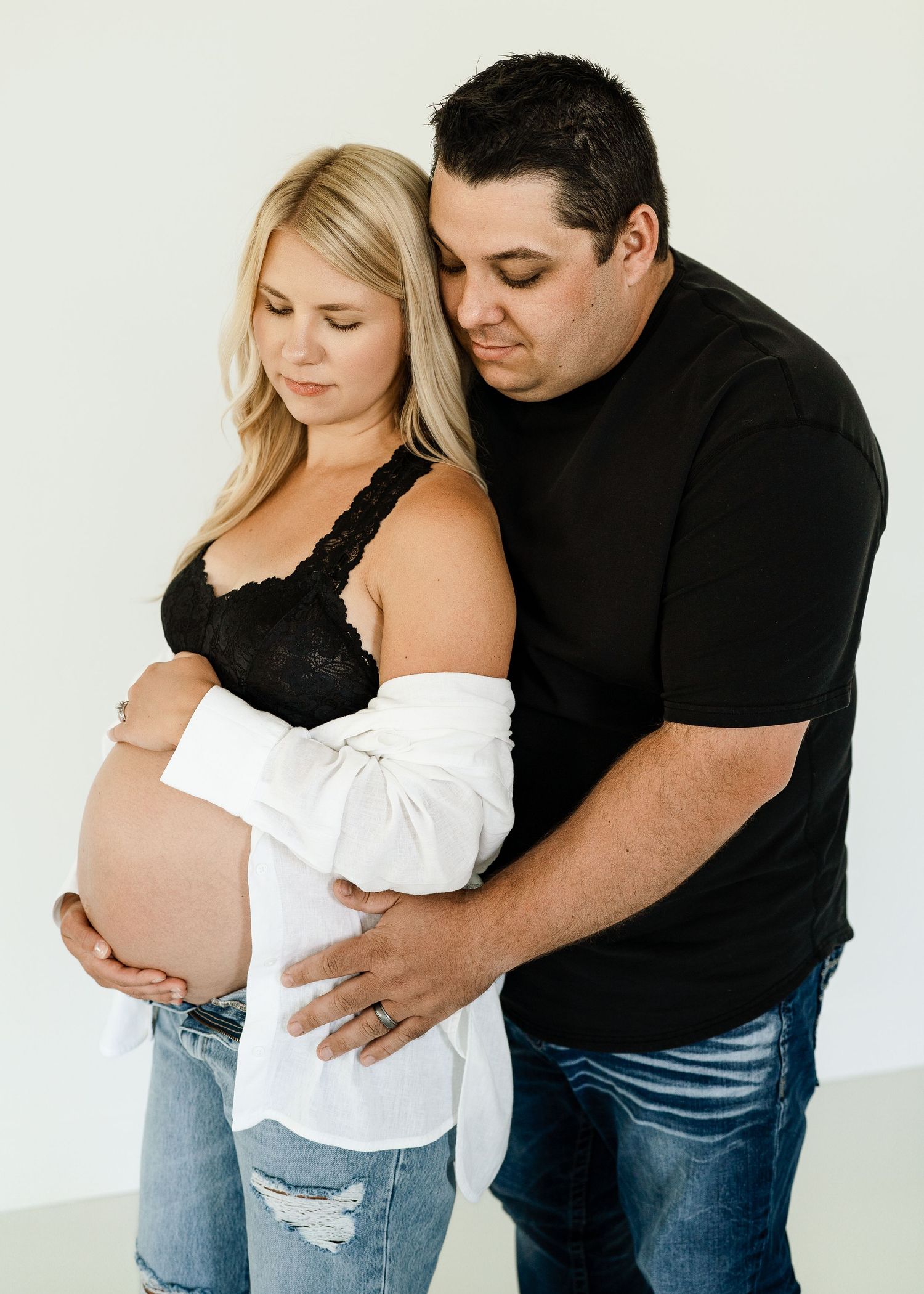 Intimate maternity portrait of couple embracing against white studio background.