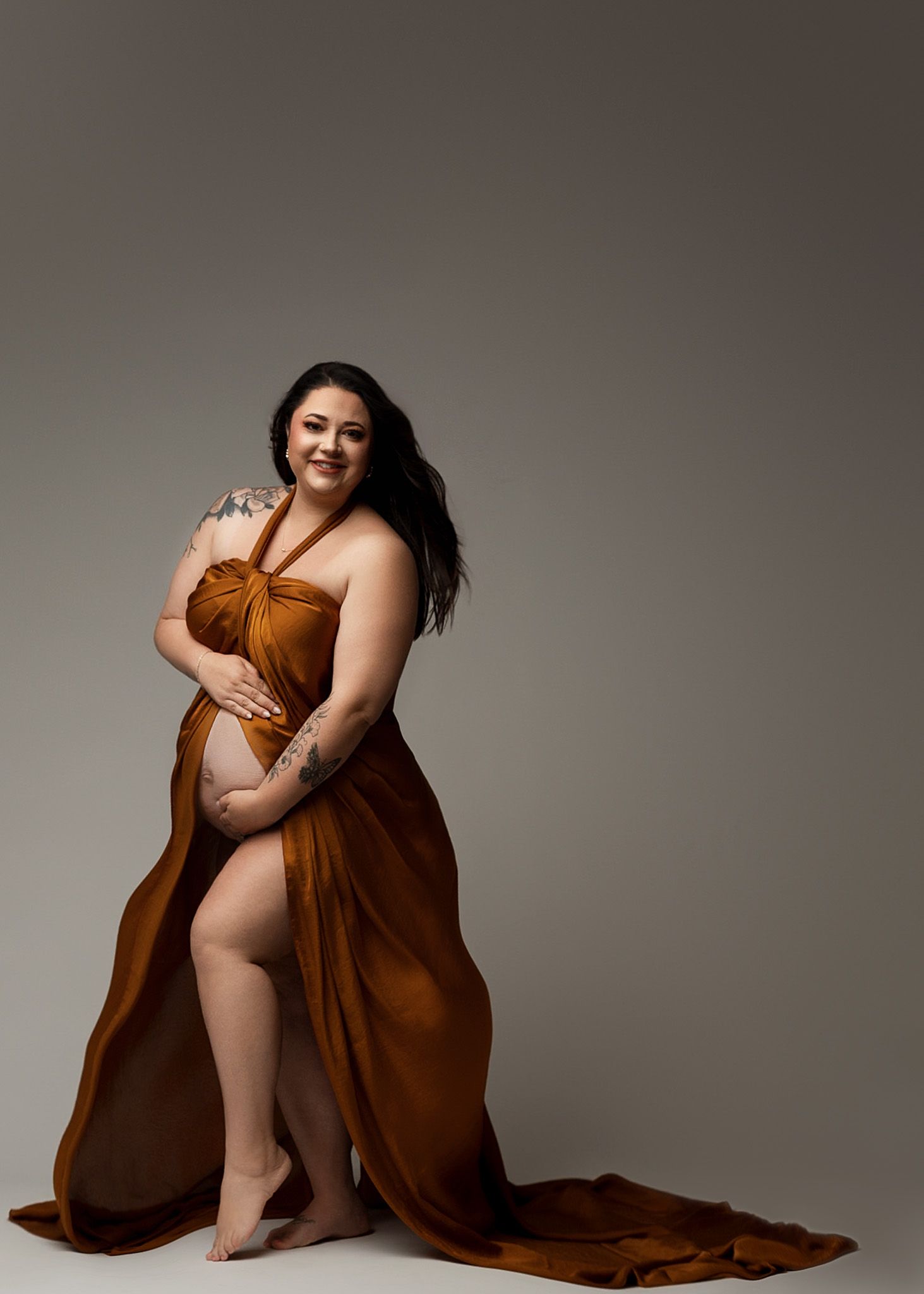 Rust-colored flowing dress with dramatic train creates elegant silhouette in studio portrait.