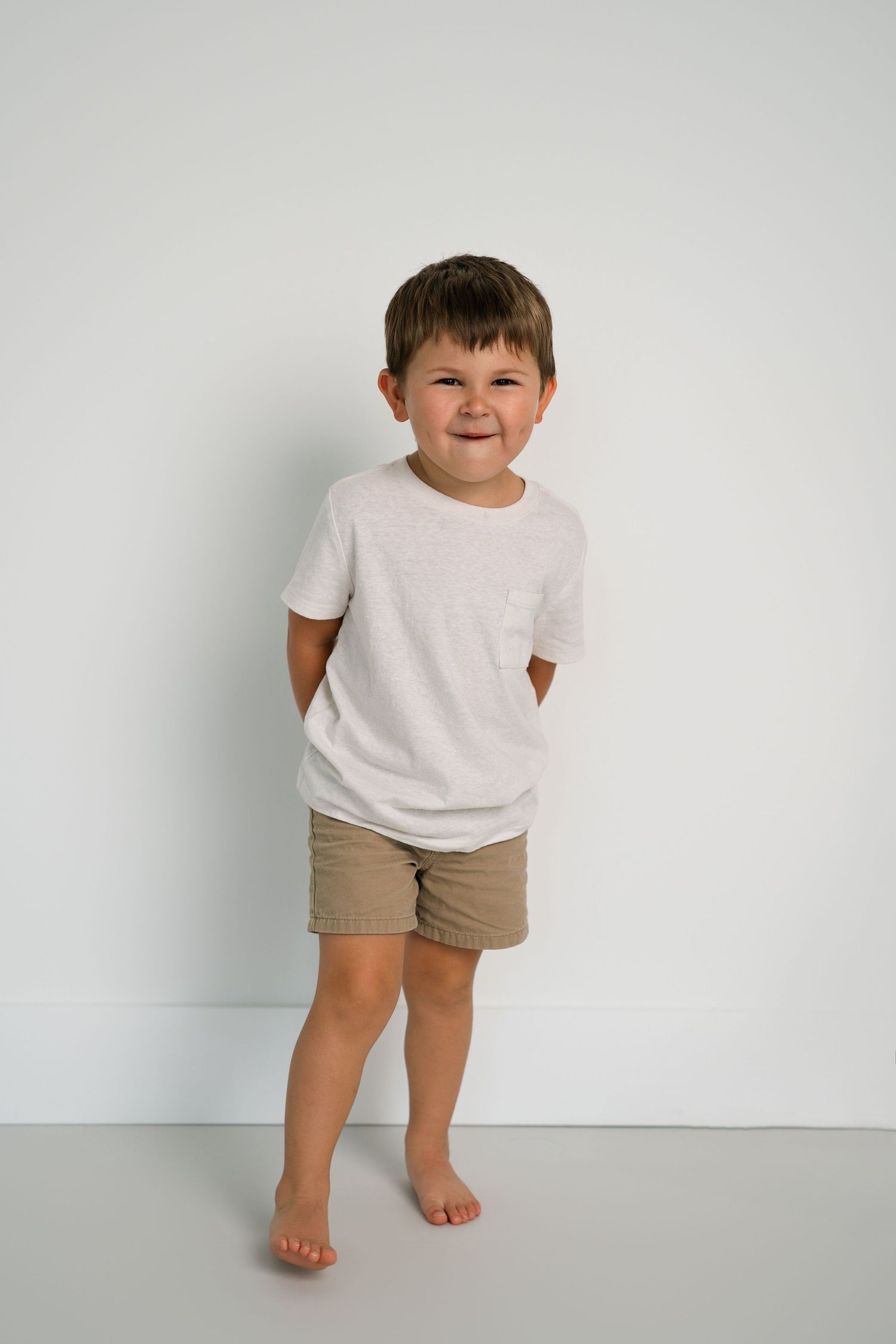 Child in white t-shirt and beige shorts poses playfully against white background.