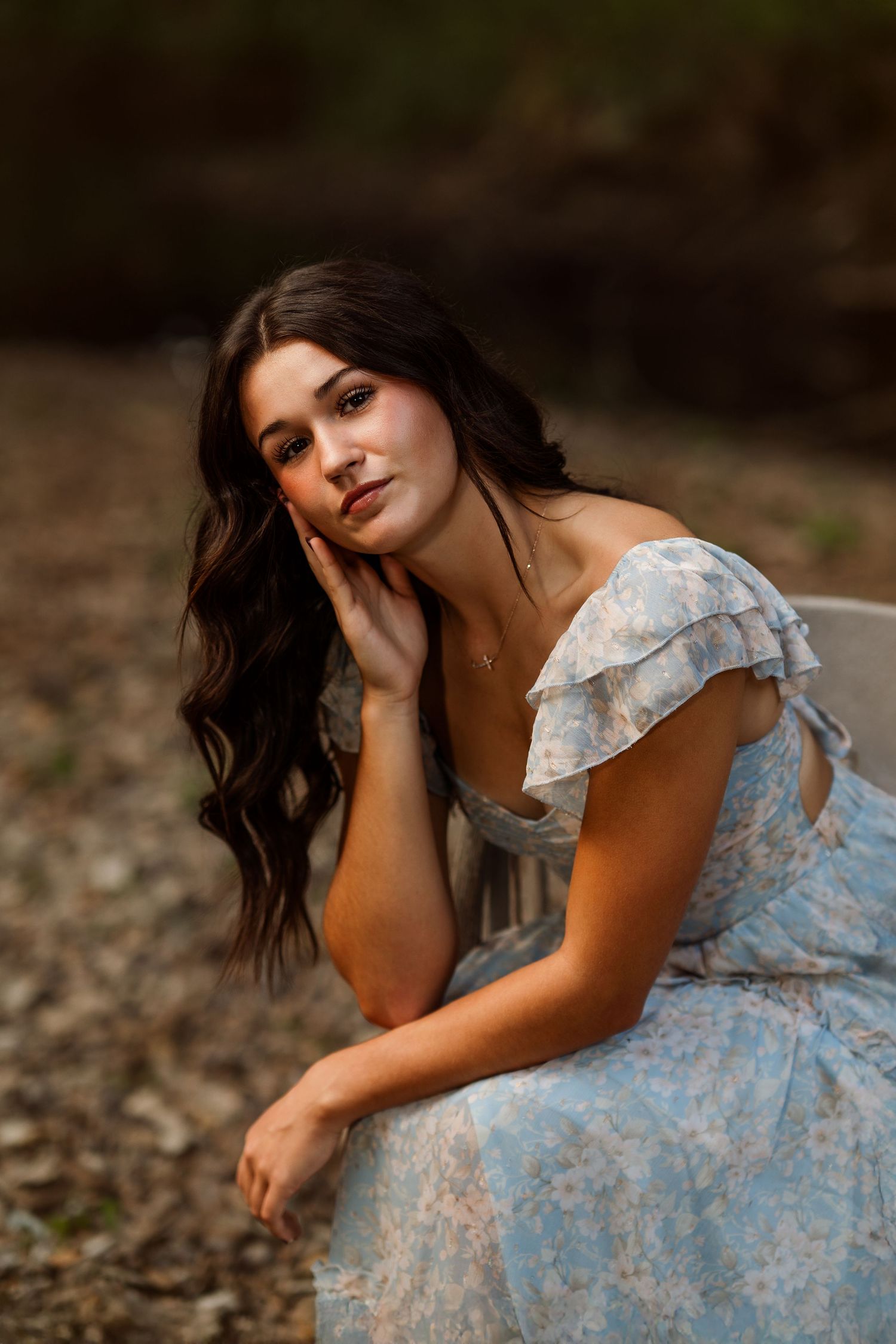 A woman in a light blue vintage dress poses artistically in a natural setting.