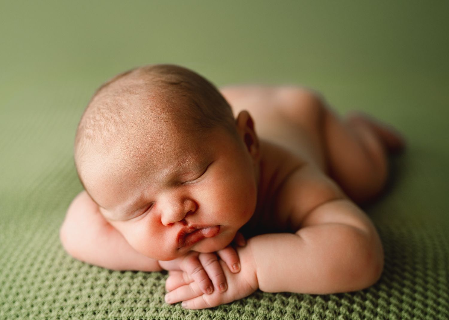 Sleeping newborn posed on textured green knit blanket.