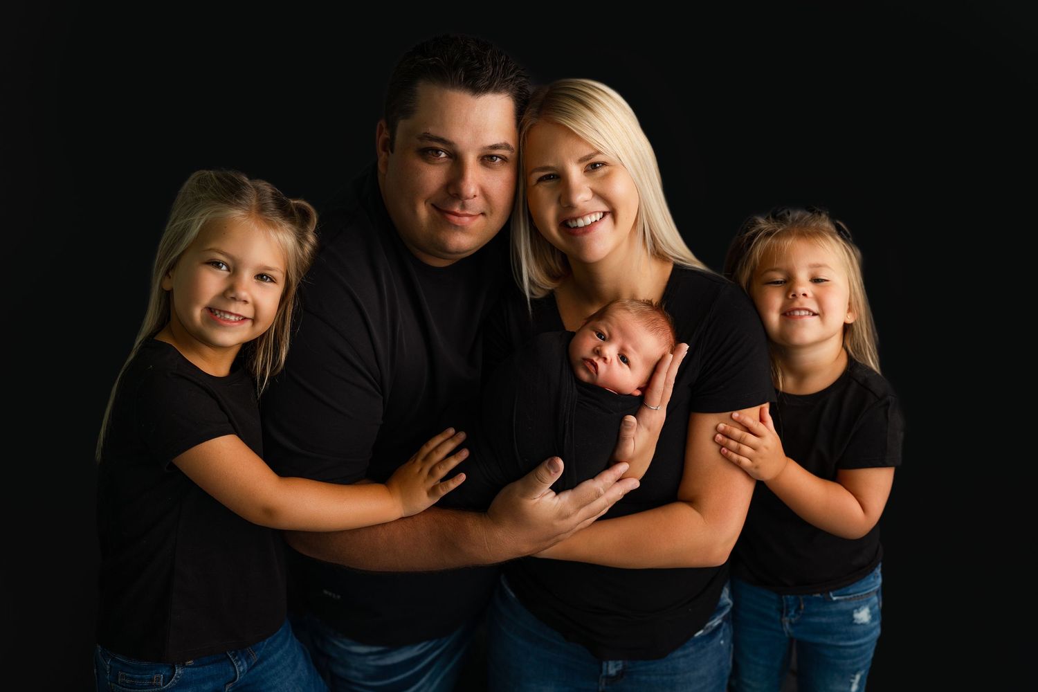 Studio family portrait with black background and coordinated casual outfits.