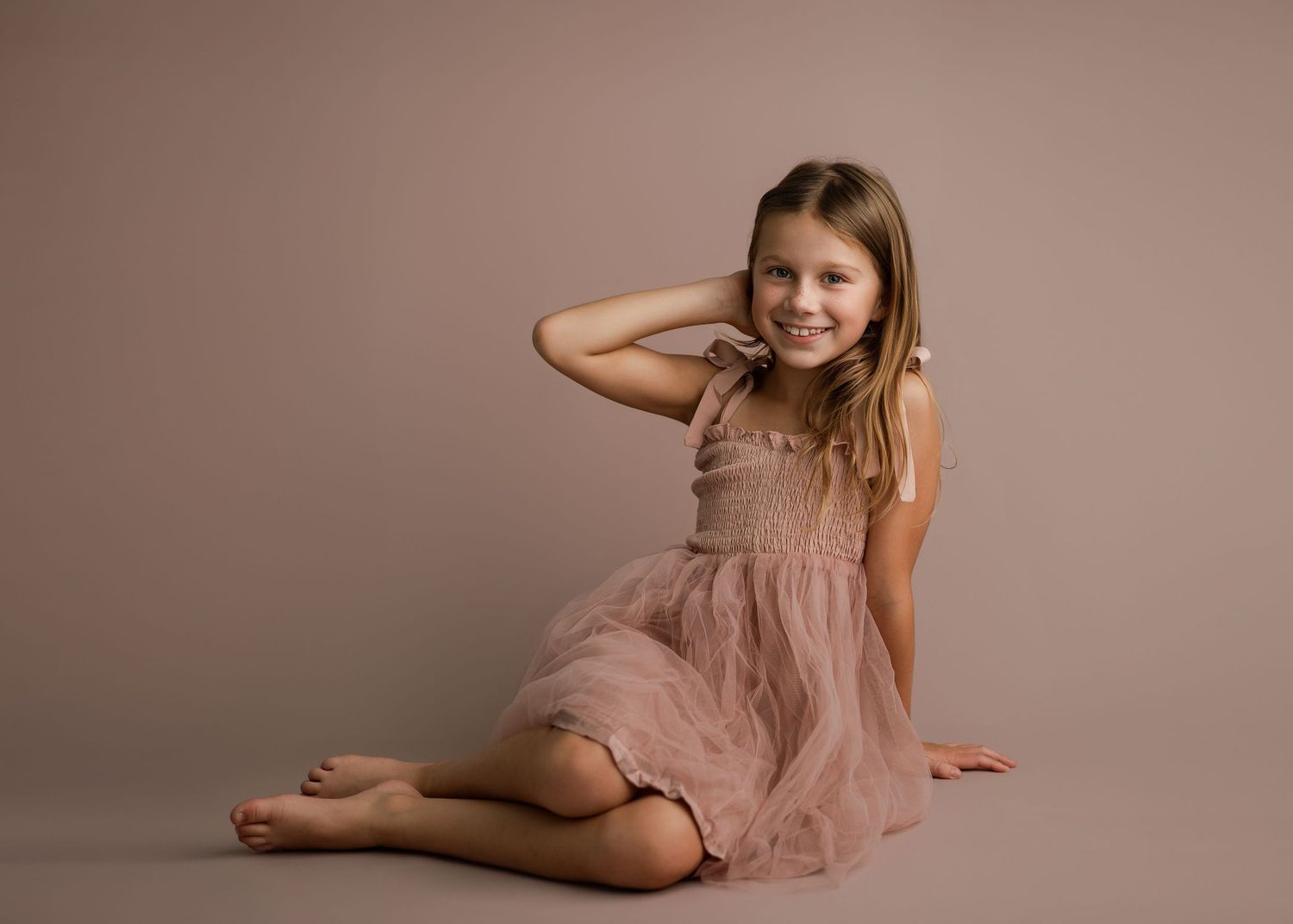 Dancer in flowing pink dress shows graceful movement against neutral studio backdrop.