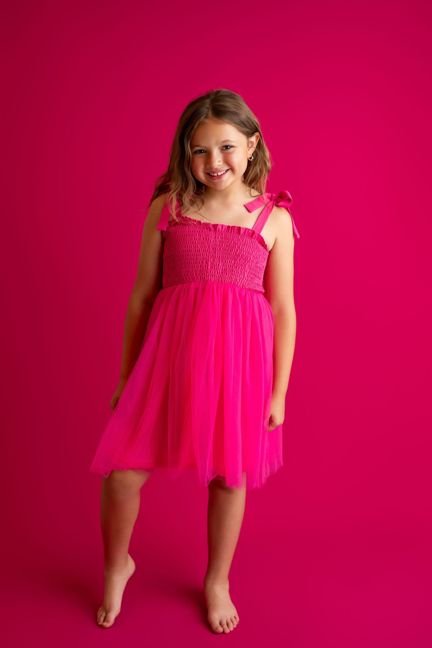 A child in a bright pink dress poses against a vibrant fuchsia background.