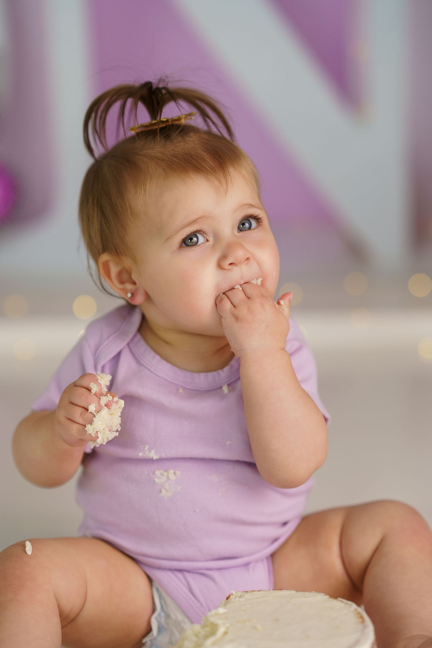 Baby in lavender outfit tasting cake during first birthday photoshoot.