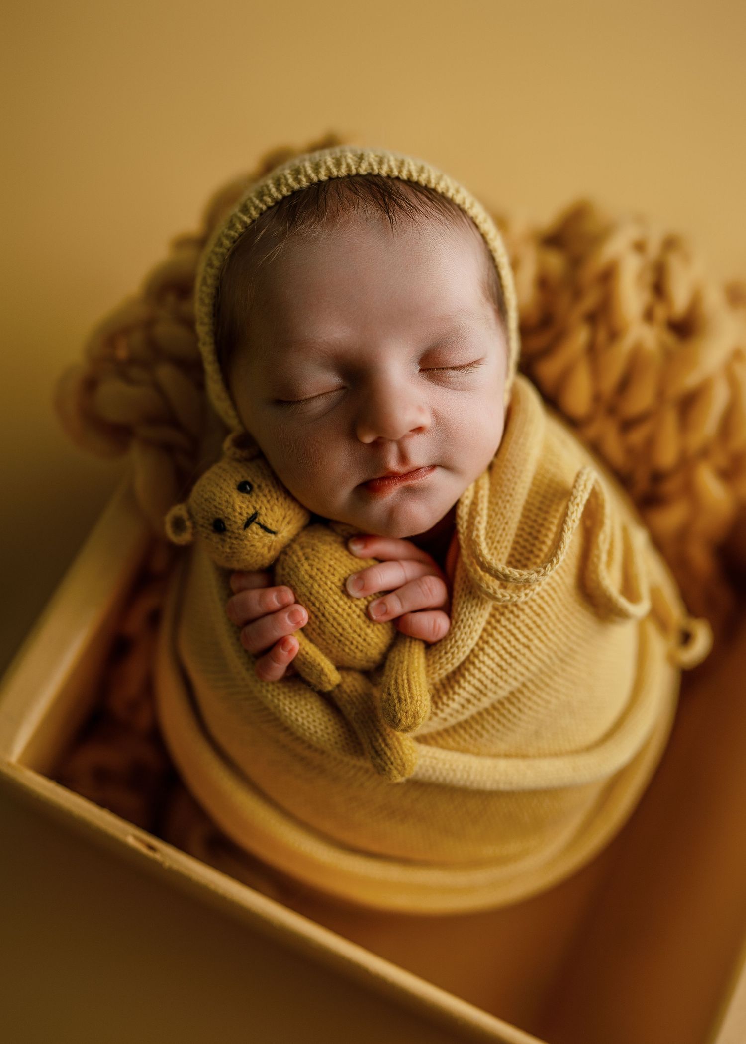 Newborn baby nestled in cozy yellow wrap during professional photography session.