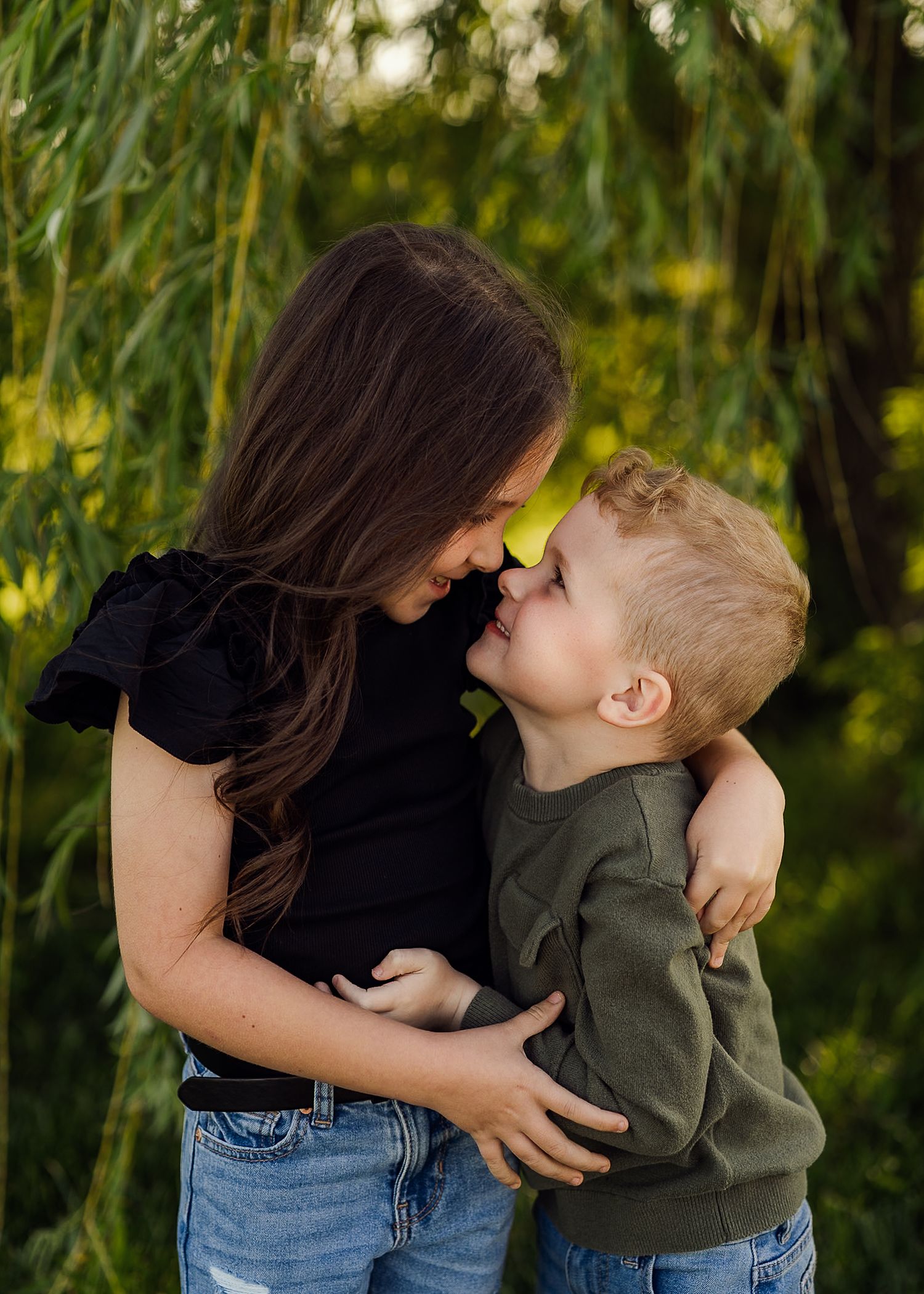 Sweet outdoor family moment captured under willow trees in natural lighting.