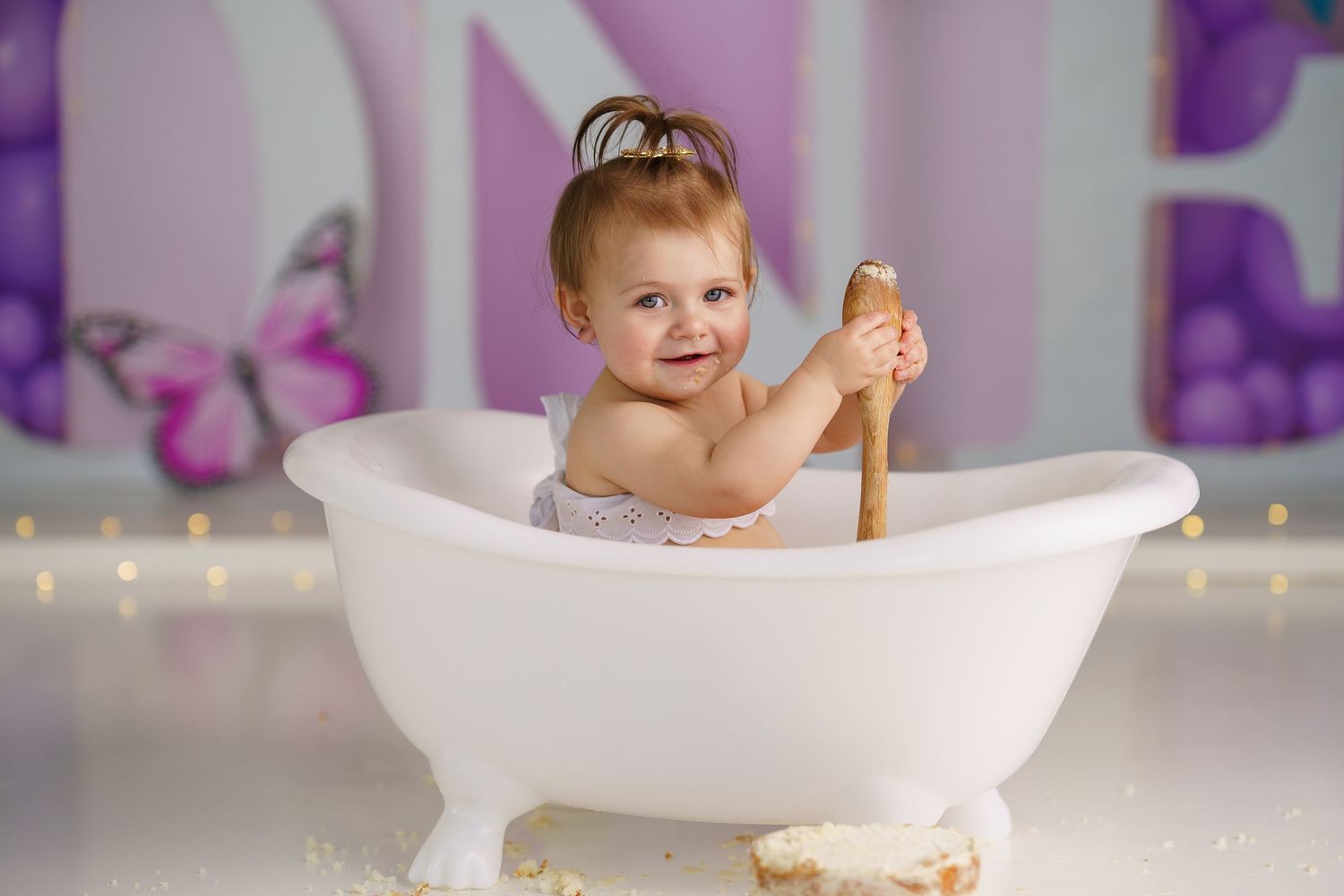 Baby sitting in miniature white bathtub during cake smash cleanup photo session.