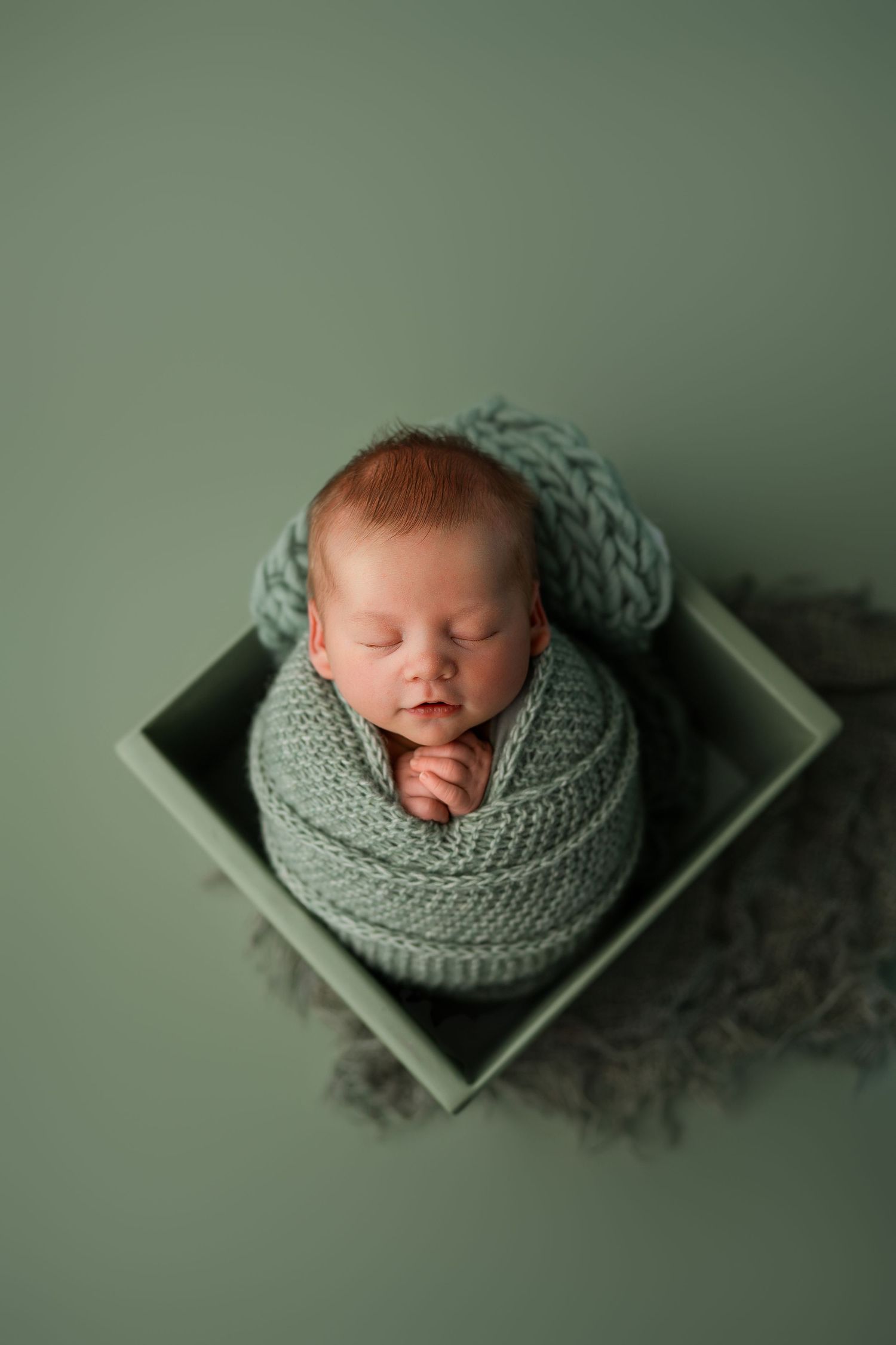 Peaceful newborn baby swaddled in soft mint green knit wrap during studio photography session.