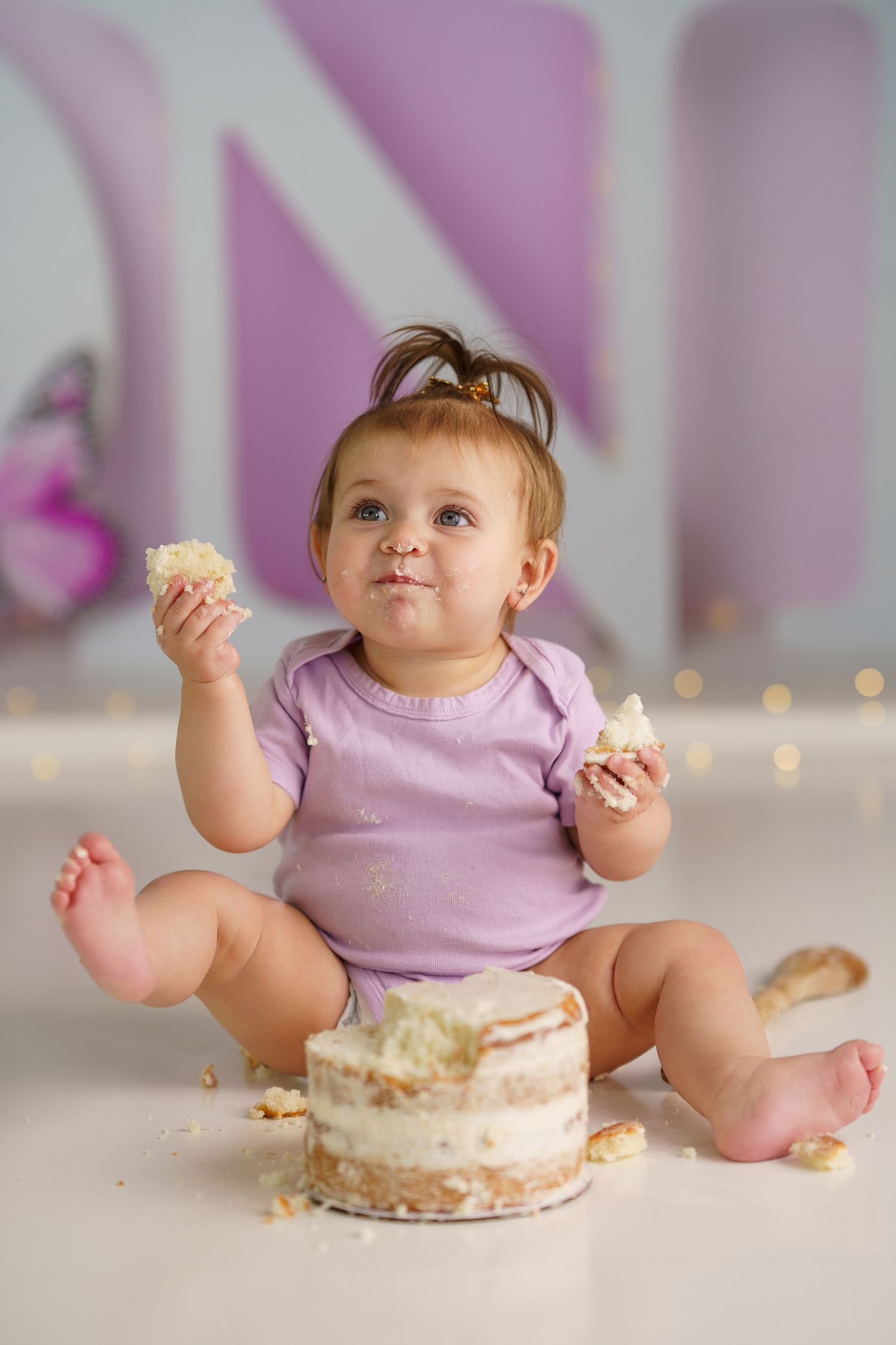 Baby in purple outfit playing with cake during first birthday photo session.