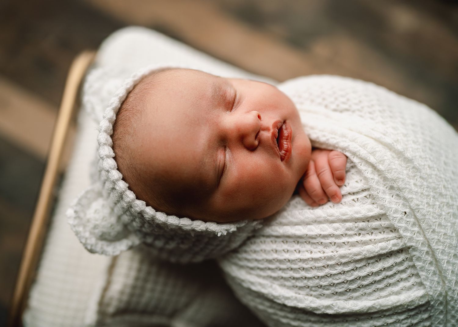 Close-up of sleeping newborn wrapped in white knitted blanket.